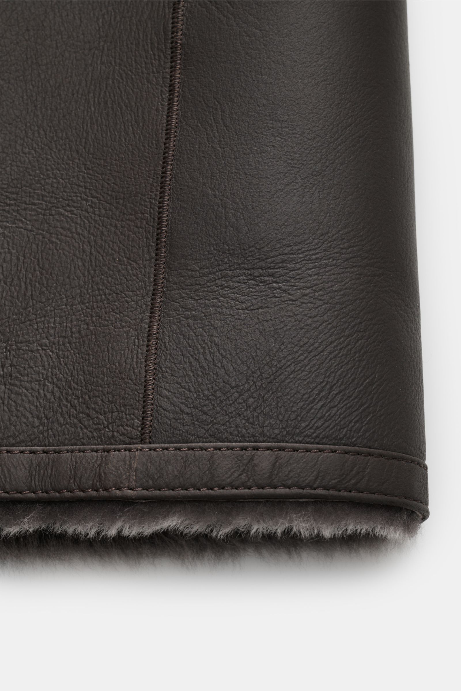 Manzoni 24 Lammfellmantel graubraun, Nahaufnahme Saum von außen mit weichem Lammleder, Lammfell-Innenseite, Slim Fit, Reverskragen, Drei-Knopf-Leiste.