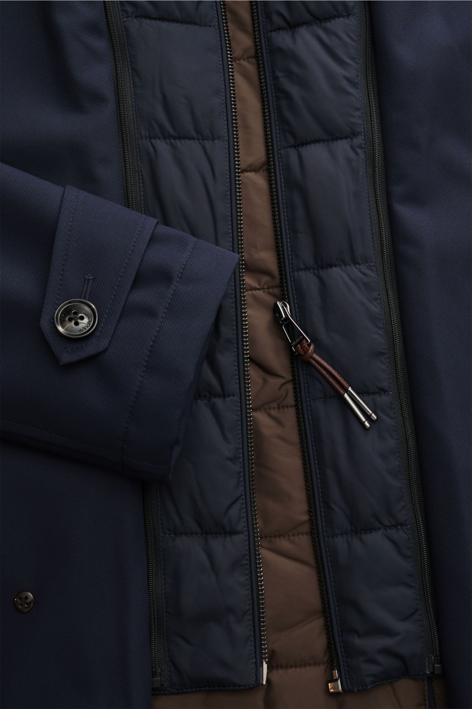 Close-up top-down view of the navy Windsor Parka 'Sarno' showing the cuff with button, quilted inner lining, and zipper with leather pull tab. Flexibel bleiben – mit Stil: Der Parka 'Sarno' von WINDSOR passt sich Ihren Ansprüchen im Handumdrehen an. Sowoh