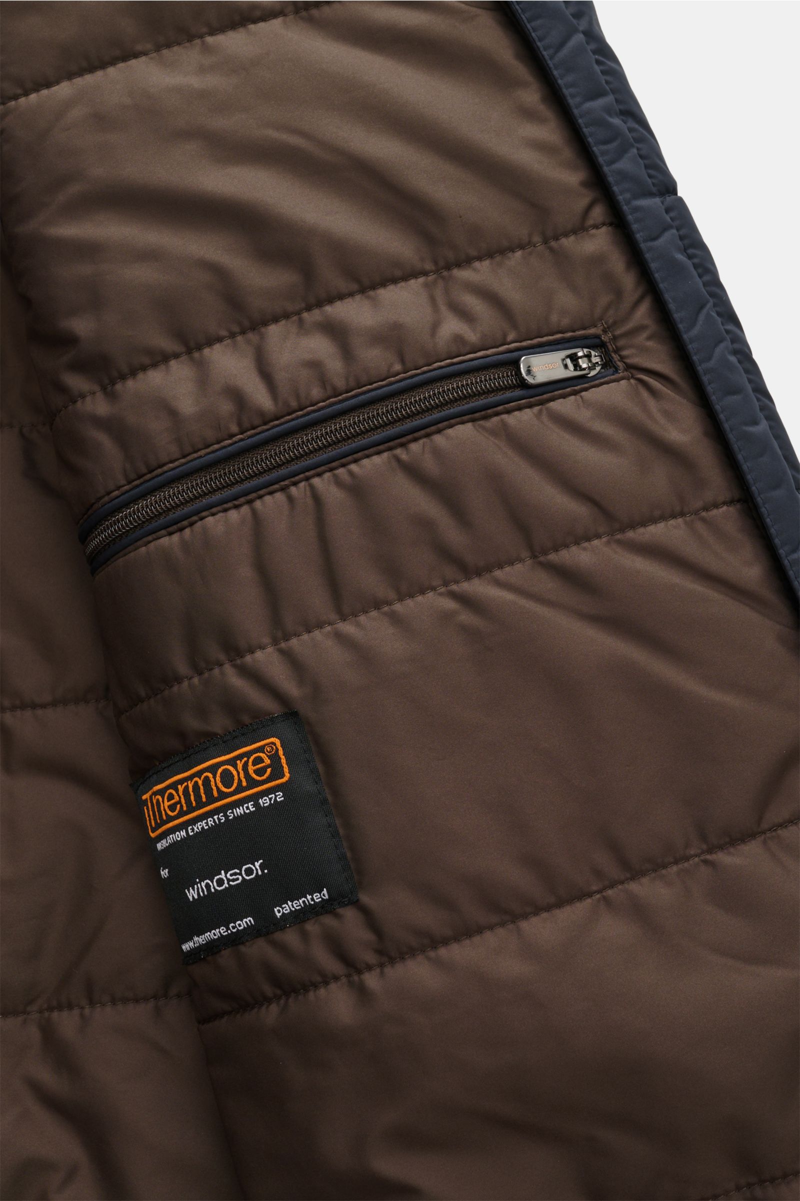 Close-up view of the brown quilted inner lining of the Windsor Parka 'Sarno' navy, showing a zippered pocket and Thermore label.

Flexibel bleiben – mit Stil: Der Parka 'Sarno' von WINDSOR passt sich Ihren Ansprüchen im Handumdrehen an. Sowohl die Kapu