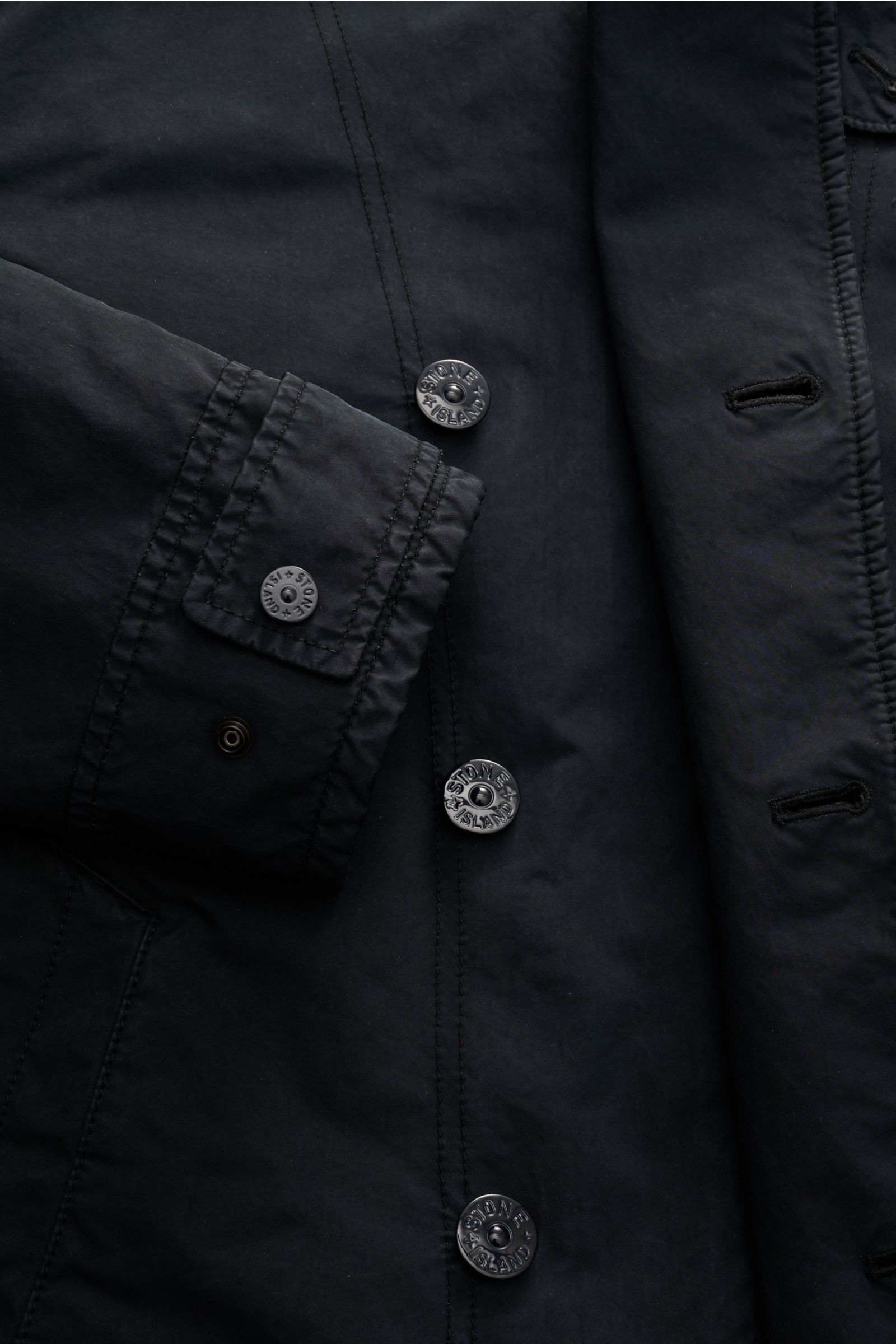 Close-up image of the Stone Island Jacke 'David-TC Ghost Piece' navy, showing the front button placket and sleeve cuff from a top-down angle. Bestens gewappnet für die Übergangszeit: Die leicht gefütterte Jacke 'David-TC' von STONE ISLAND ist mit ihrem so