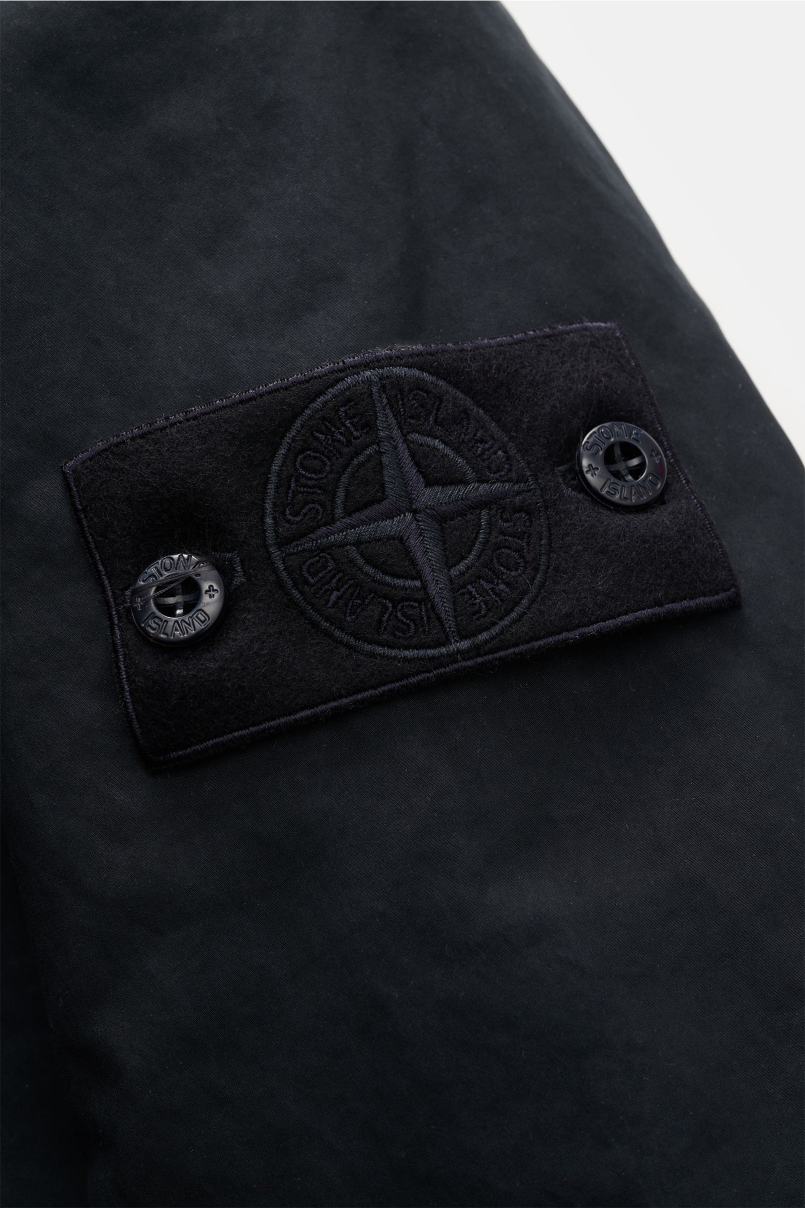 Close-up from a side angle of the tonal compass badge on the sleeve of the Stone Island Jacke 'David-TC Ghost Piece' navy, a slim fit, lightly padded jacket with robust cotton, Anti-Drop-Finish, and soft touch, designed for transition seasons with water- 
