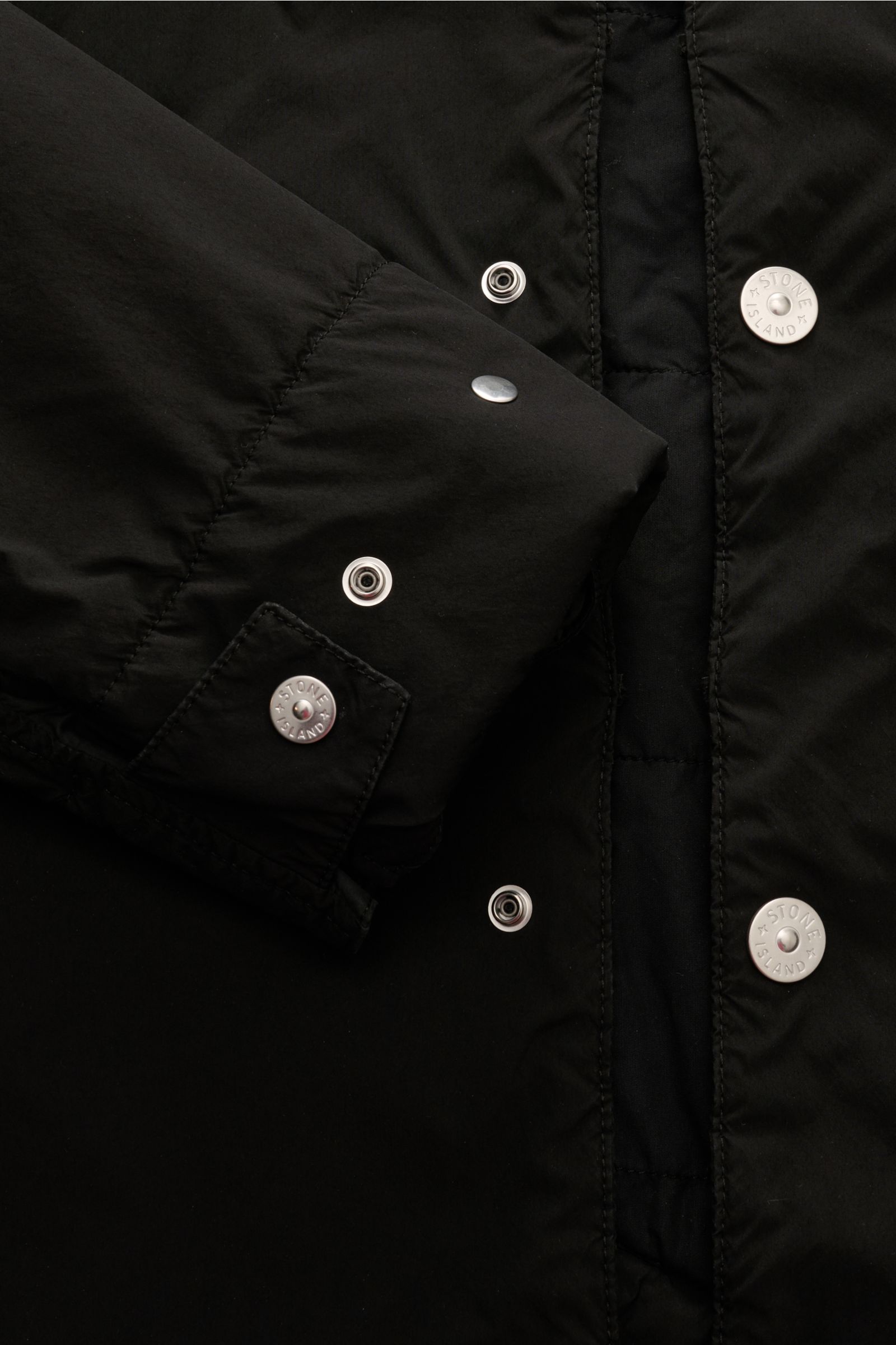 Stone Island Parka 'Light Compact Touch Poly-TC' schwarz, Detailaufnahme von Knopfleiste und Ärmel mit Kompass-Badge, wind- und wasserabweisend.