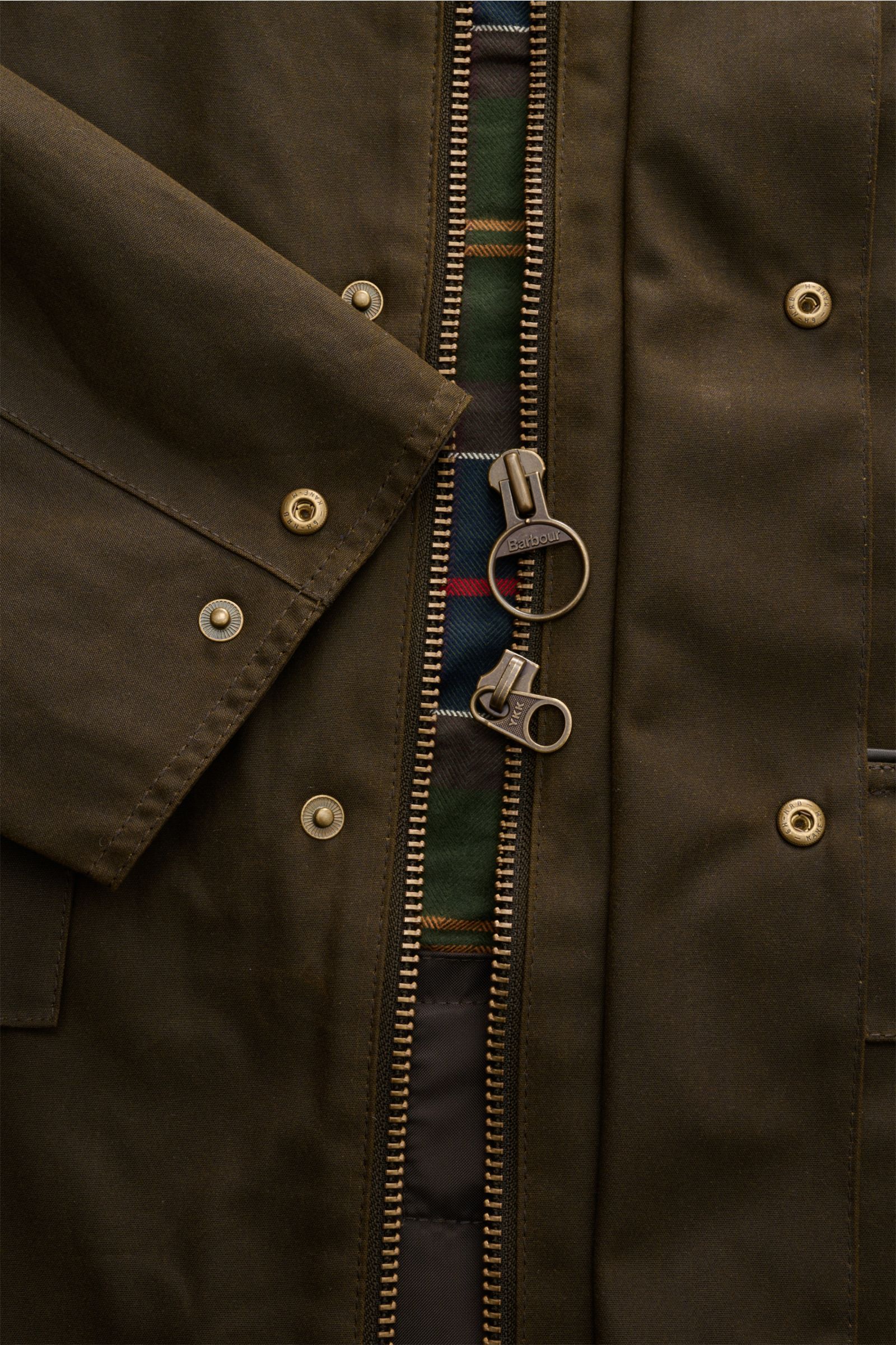 Nahaufnahme des Barbour Wachsparka 'Country' dark olive von vorne, zeigt gewachste Baumwolle, zwei-Wege-Reißverschluss mit Tartan-Futter.