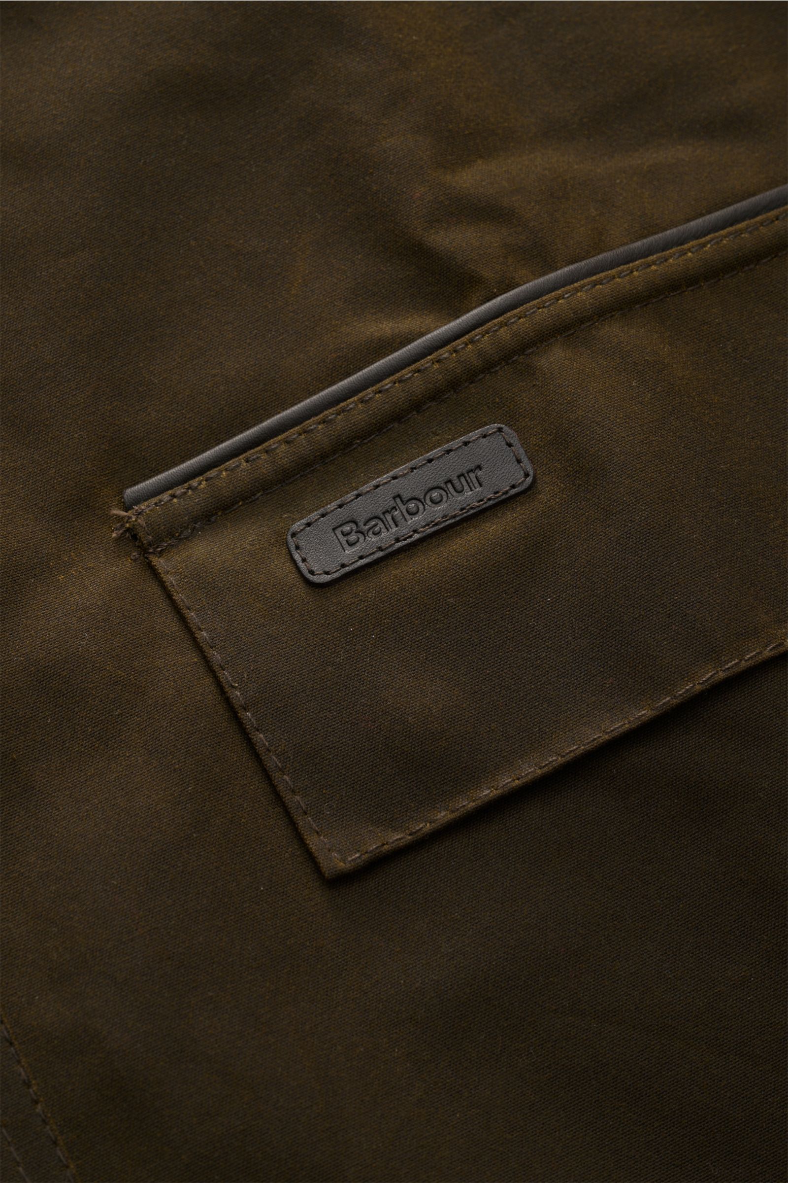 Nahaufnahme des Barbour Wachsparka 'Country' dark olive mit gewachster Baumwolle, aufgesetzter Tasche und Logo, wasserabweisend.