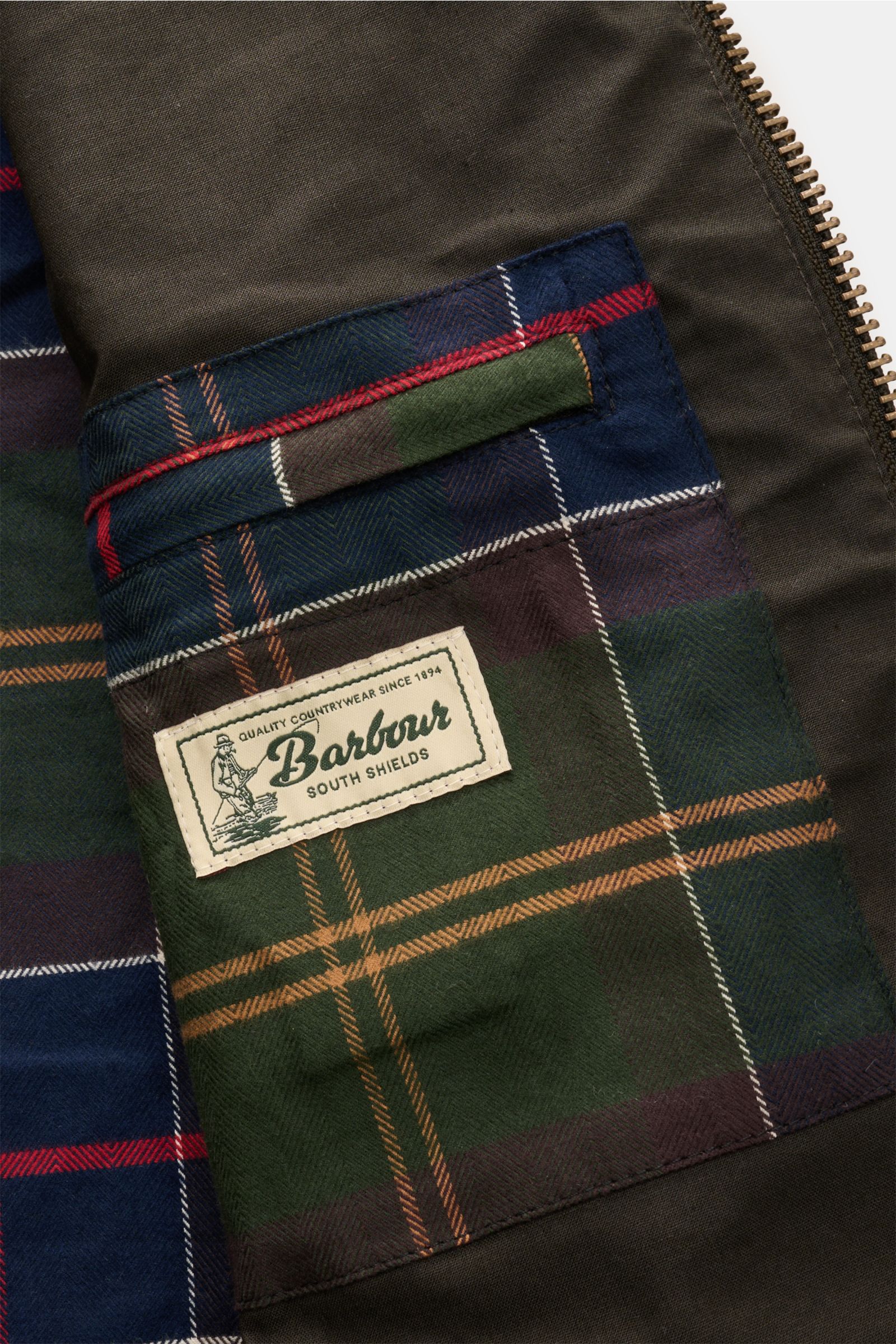 Detailansicht des typischen Tartan-Futters und der Innentasche im Barbour Wachsparka 'Country' dark olive aus gewachster Baumwolle.