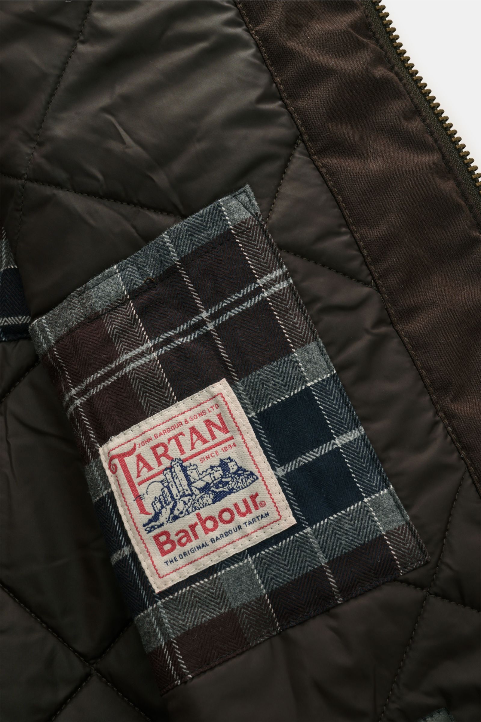 Nahaufnahme des gesteppten Innenfutters mit Barbour Tartan-Label im Barbour Wachsparka 'Beaudale' khaki aus gewachster Baumwolle.