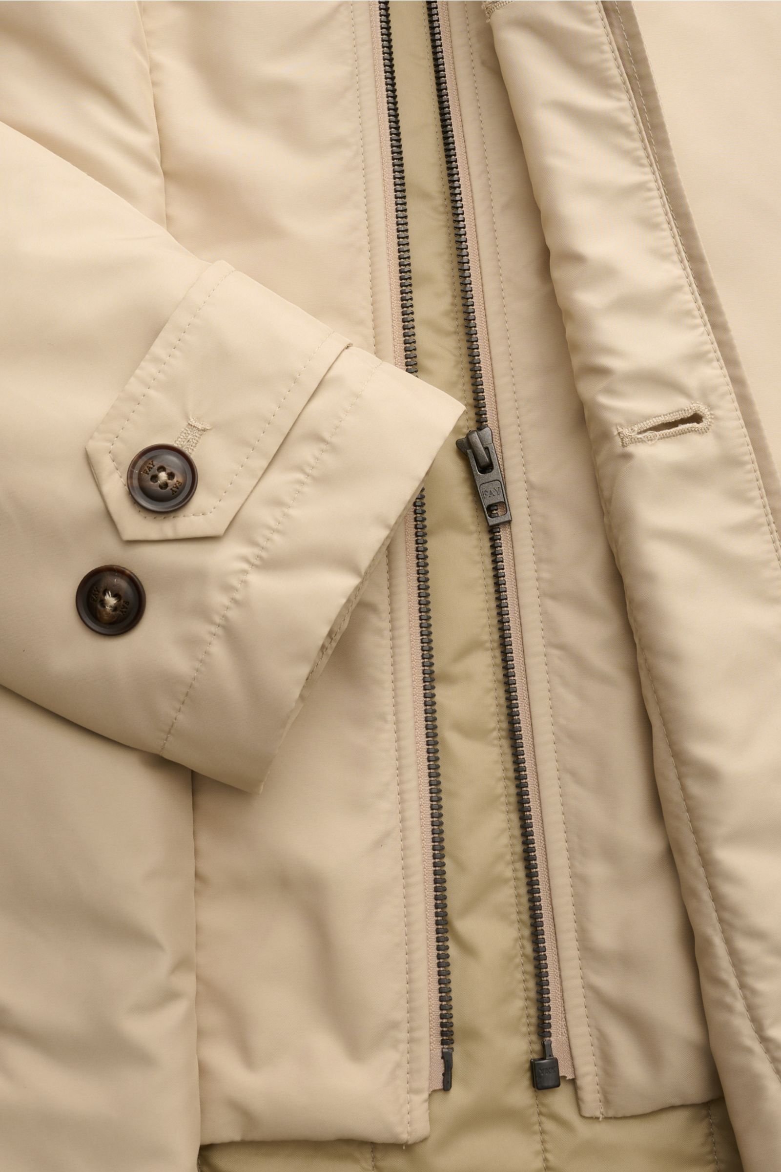 Close-up front view of the Fay Mantel 'Morning Coat' beige showing the smooth popeline technical microfiber fabric, robust zipper, buttoned wind flap, adjustable cuff with two buttons, and quilted lining.  
 

Popeline aus technischer Micro