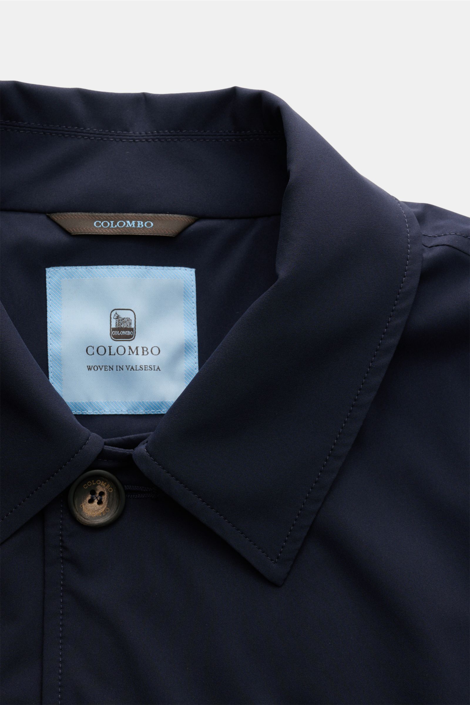 Close-up front view of Colombo Mantel navy collar and button, made from high-quality microfiber with smooth touch.

Description: Dieser Mantel aus hochwertiger Microfaser vom Traditionshaus COLOMBO verkörpert Luxus in seiner reinsten Form und wird durc