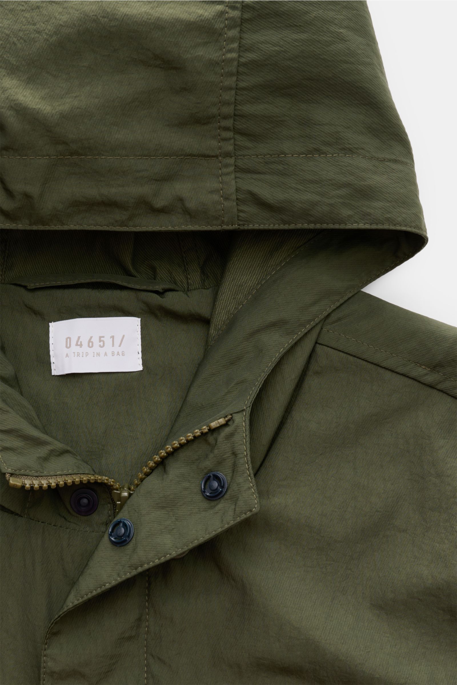 Nahe Aufnahme des olivfarbenen 04651/ A trip in a bag Mantel 'Travel Coat' mit Kapuze, Reißverschluss und Druckknöpfen, wasserabweisend und winddicht.