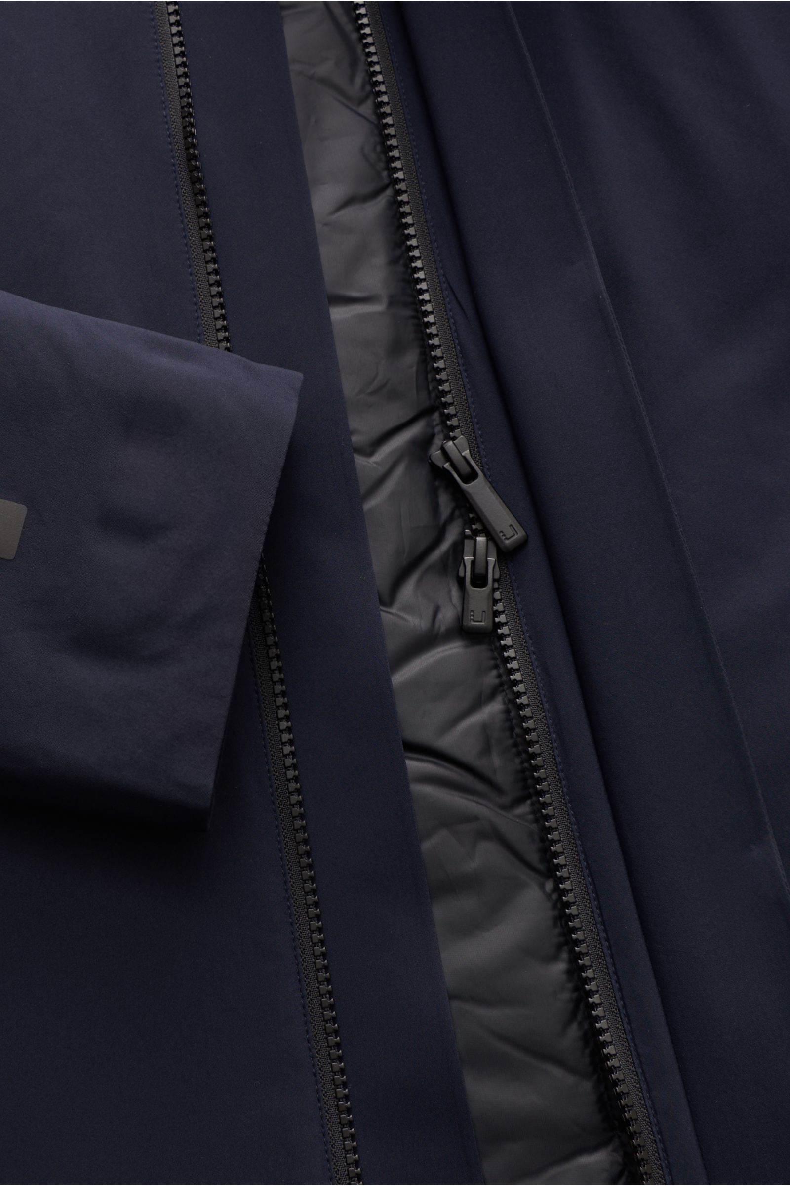 Close-up front view of the UBR Mantel 'Black Storm' navy showing the waterproof technical microfiber fabric, smooth texture, taped seams, and two-way zipper with magnetic wind flap. The removable Primaloft lining is visible inside, highlighting its breath