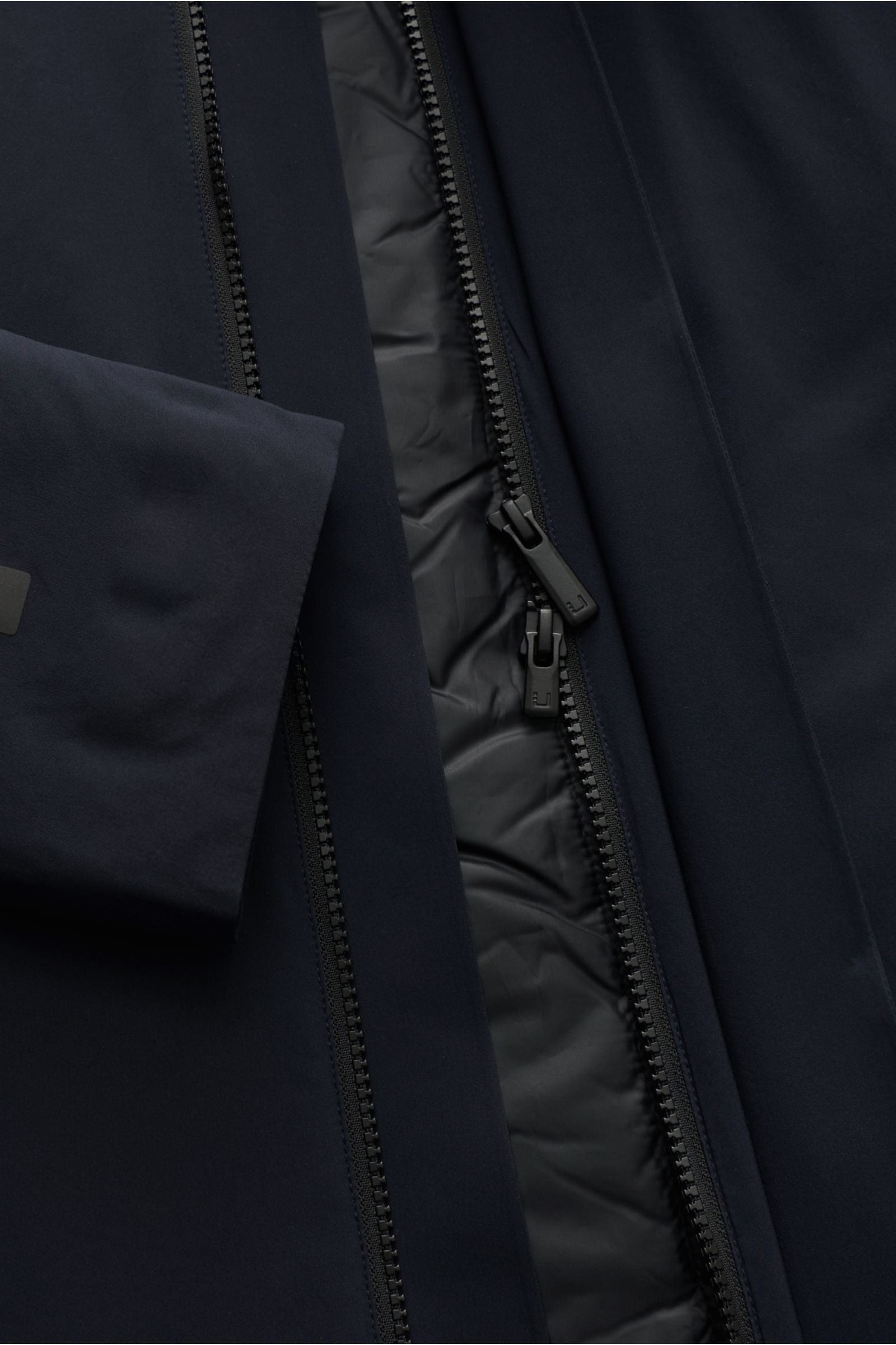 Nahaufnahme des UBR Mantels 'Black Storm' dark navy von vorne, zeigt glatte technische Microfaser, getapte Nähte und robusten Zwei-Wege-Reißverschluss.