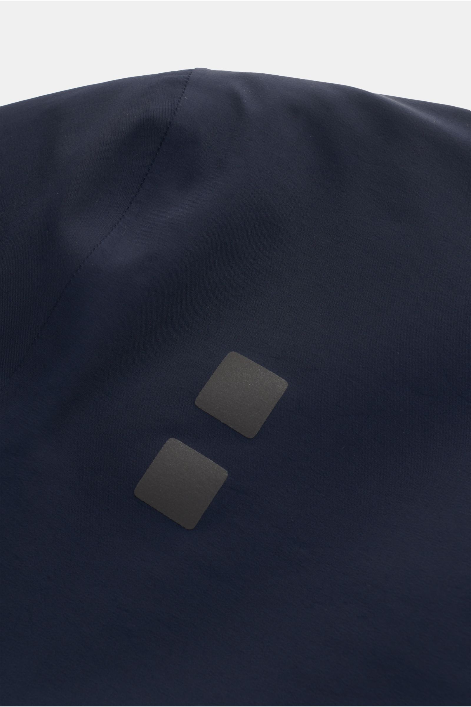 Close-up of the back of the UBR Kurzmantel 'Regulator Coat' navy showing two small reflective square prints on smooth, navy microfiber fabric.

Description: Leicht und besonders funktional ist das Modell 'Regulator Coat' des norwegischen Labels UBR – skan