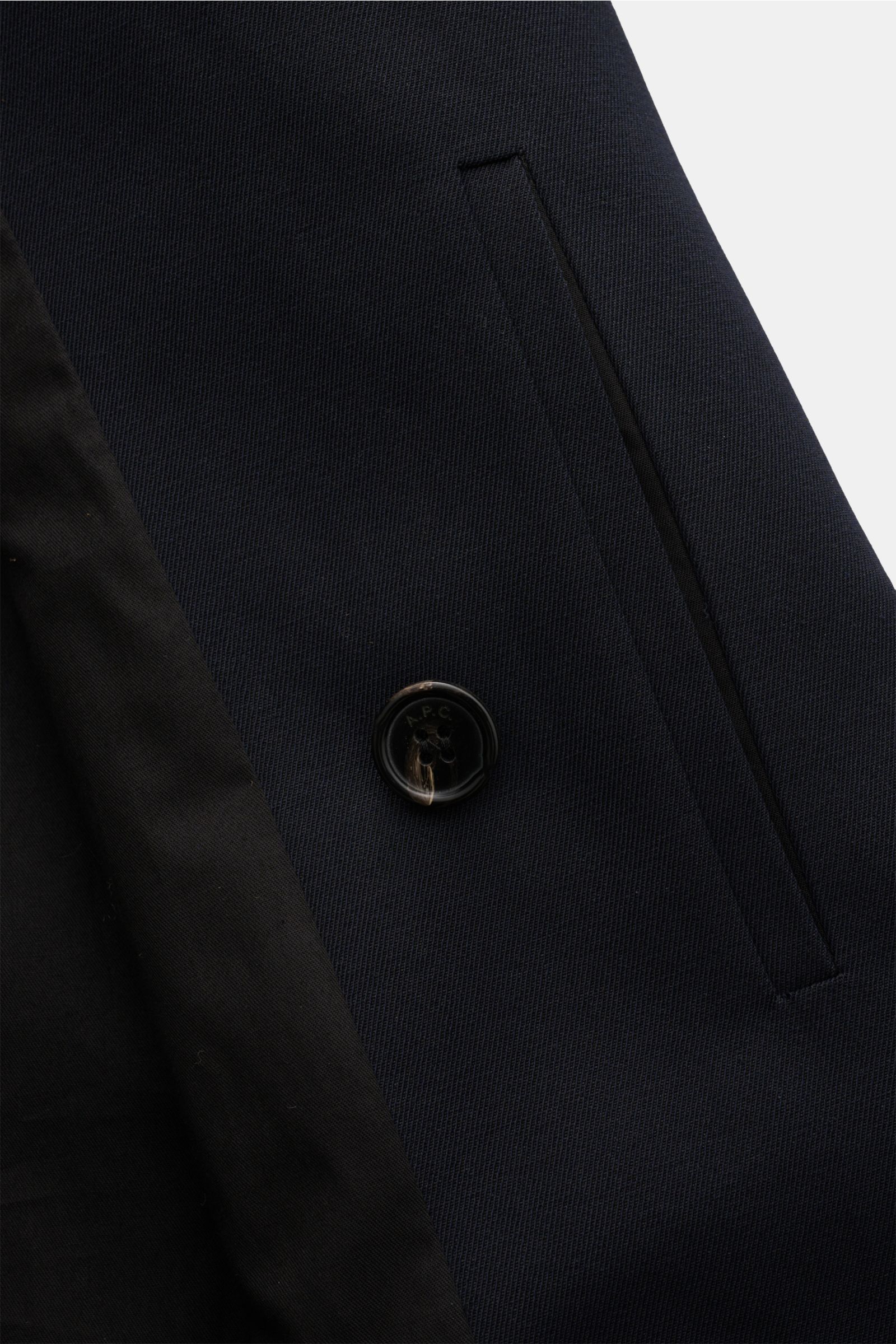 Nahaufnahme des A.P.C. Mantel navy aus Baumwoll-Woll-Mix, schlanker Slim Fit, zweireihiger Drei-Knopf-Stil, fallendes Revers, schräge Leistentasche, innen schwarzes Futter.