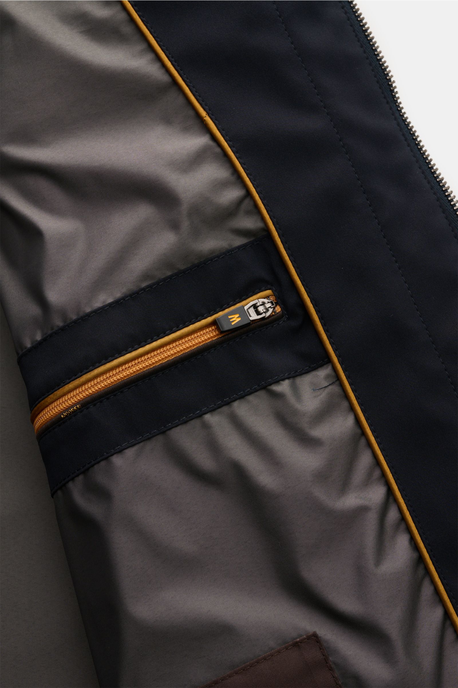 Close-up interior view of the Moorer Kurzmantel 'Borromini' navy showing the smooth lining, brown zippered inner pocket with orange trim, and part of the water-repellent outer shell.