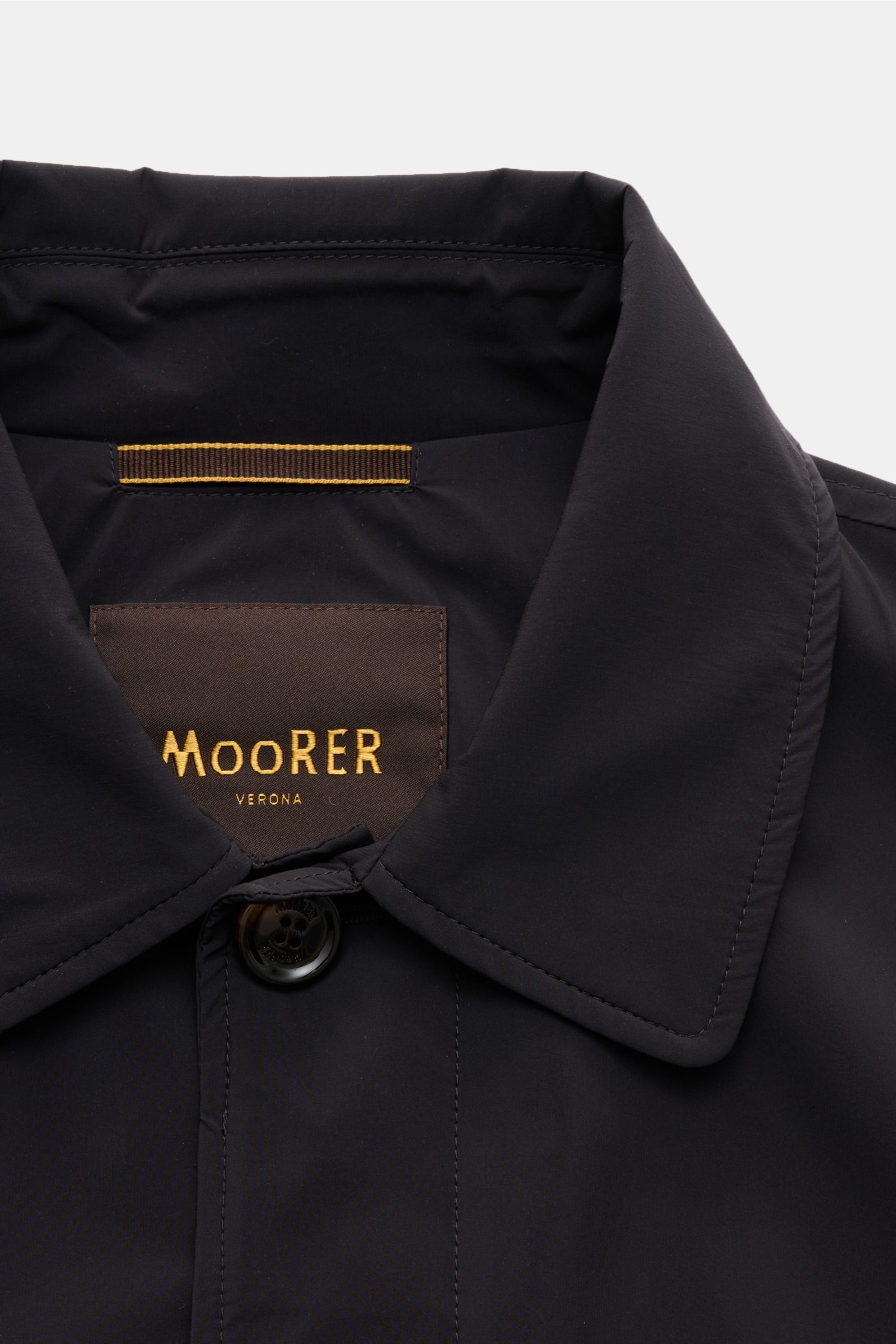 Close-up front view of the Moorer Kurzmantel 'Vittor' navy showing its water-repellent microfiber fabric, slim fit, four-button placket, turn-down collar, piped front pockets, buttoned sleeve cuffs, back center vent, smooth lining, and inner pocket. Edles