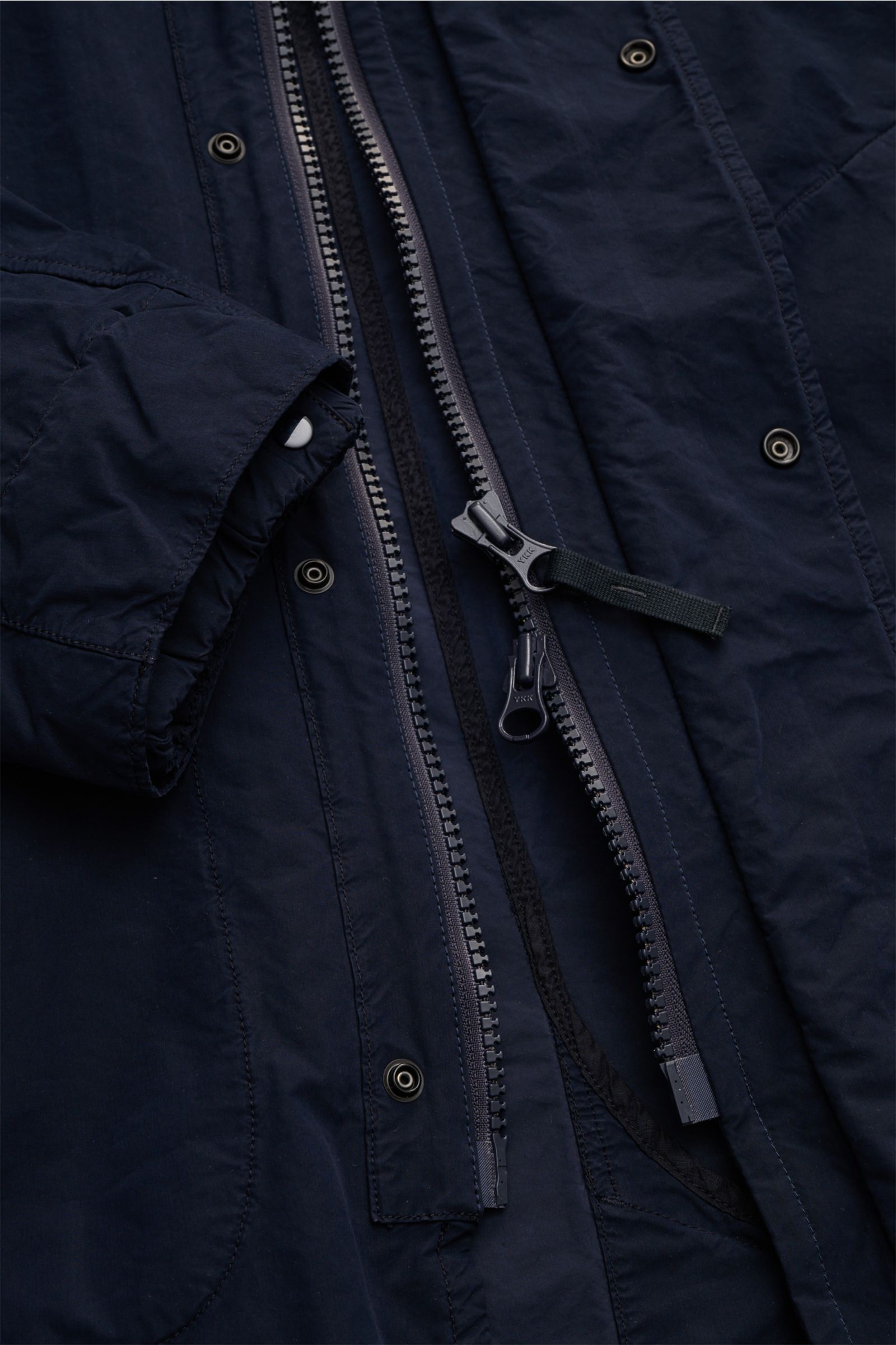 Nahaufnahme des Stone Island Mantels 'Ghost Piece' navy, von oben fotografiert, zeigt wasserabweisenden Reißverschluss, Druckknöpfe, Slim Fit, Mikrofasermaterial und Windschutzdetails.