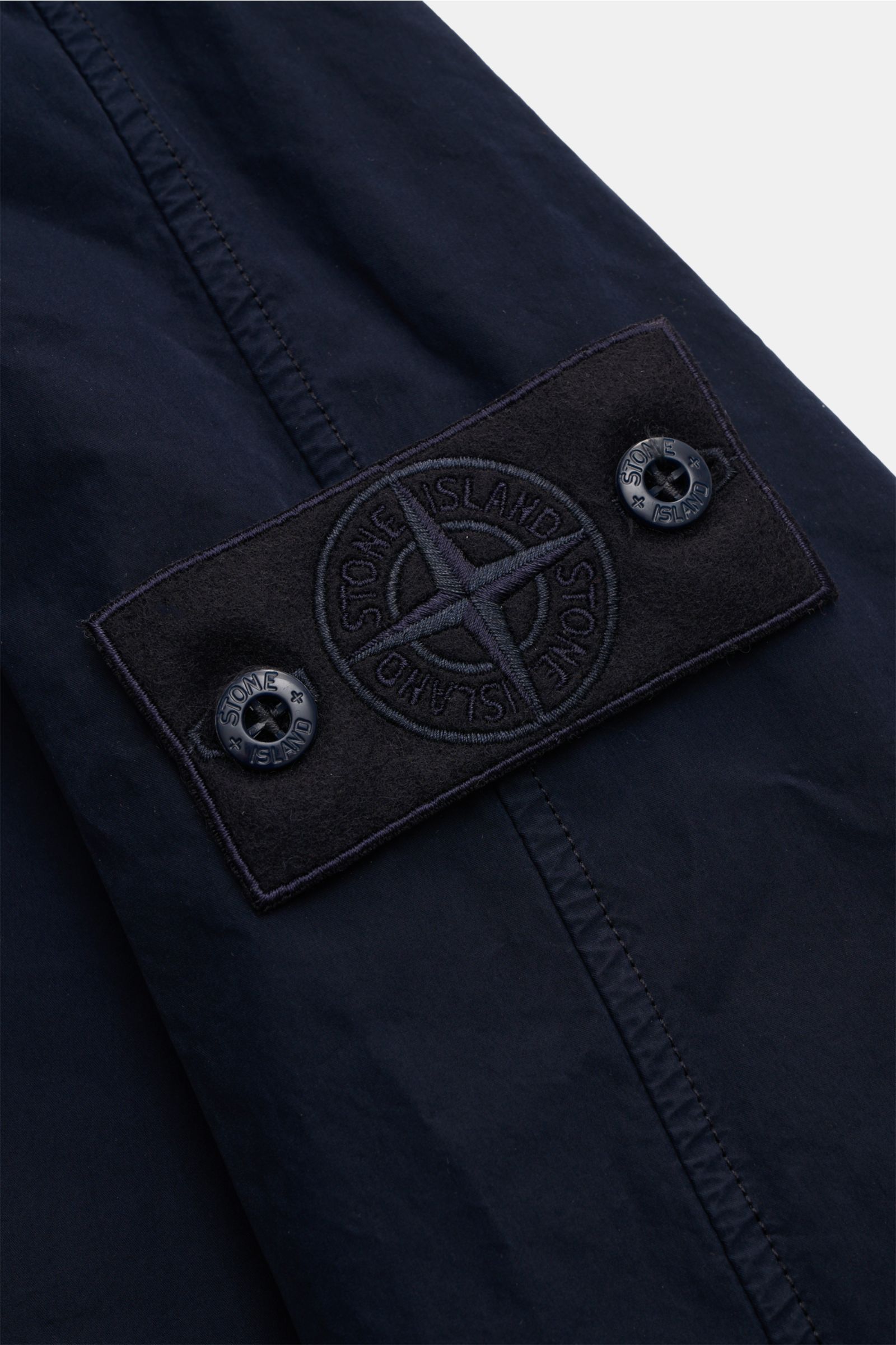 Nahaufnahme des tonalen Kompass-Badges am Ärmel des Stone Island Mantels 'Ghost Piece' navy aus hochwertiger, wasserabweisender Microfaser.