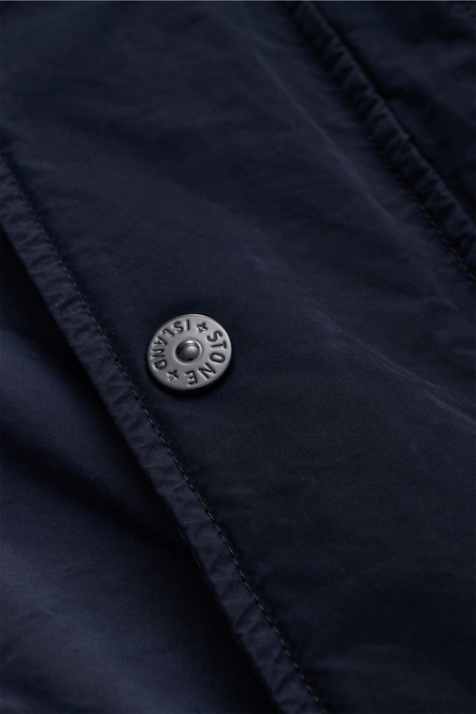 Nahaufnahme des Stone Island Mantels 'Ghost Piece' navy aus der Ghost-Collection, hochwertige Microfaser mit matt glänzendem Druckknopf.