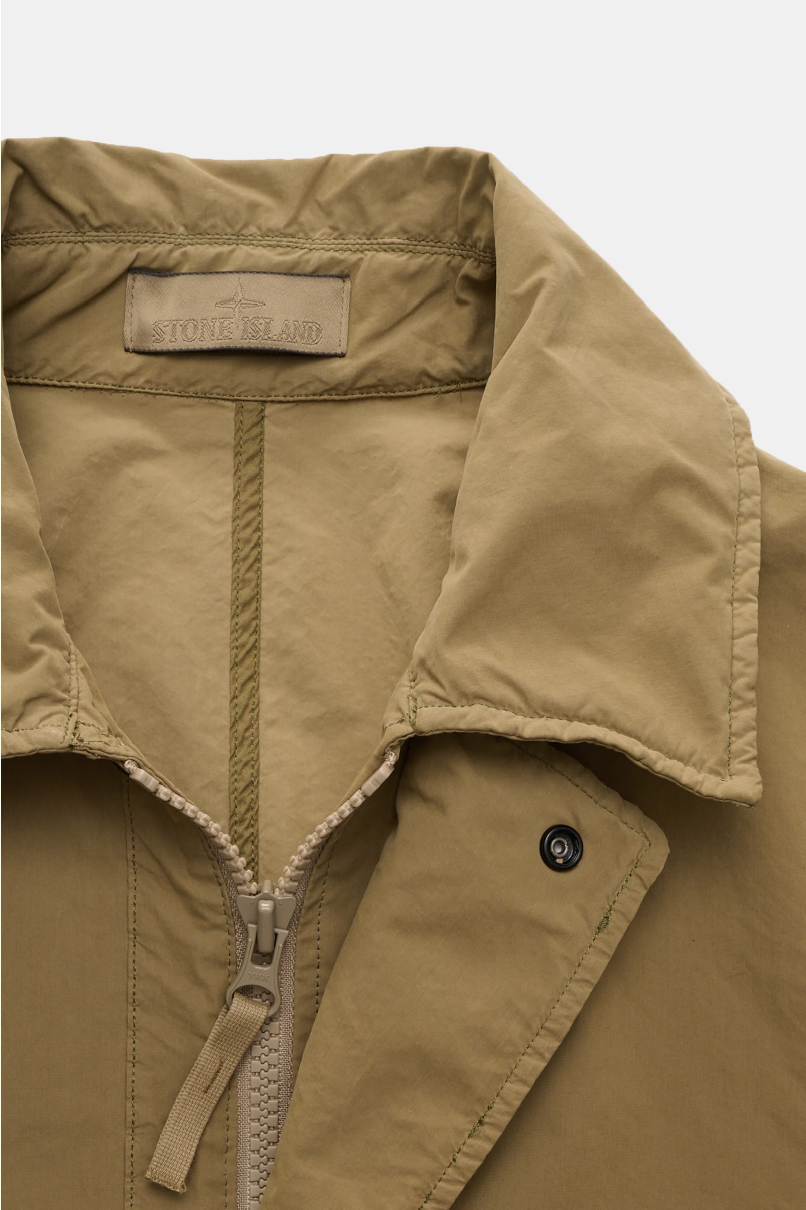 Close-up front view of the Stone Island Coat 'Ghost Piece' khaki showing the collar, two-way zip, and snap button flap in lightweight David Light-TC fabric.