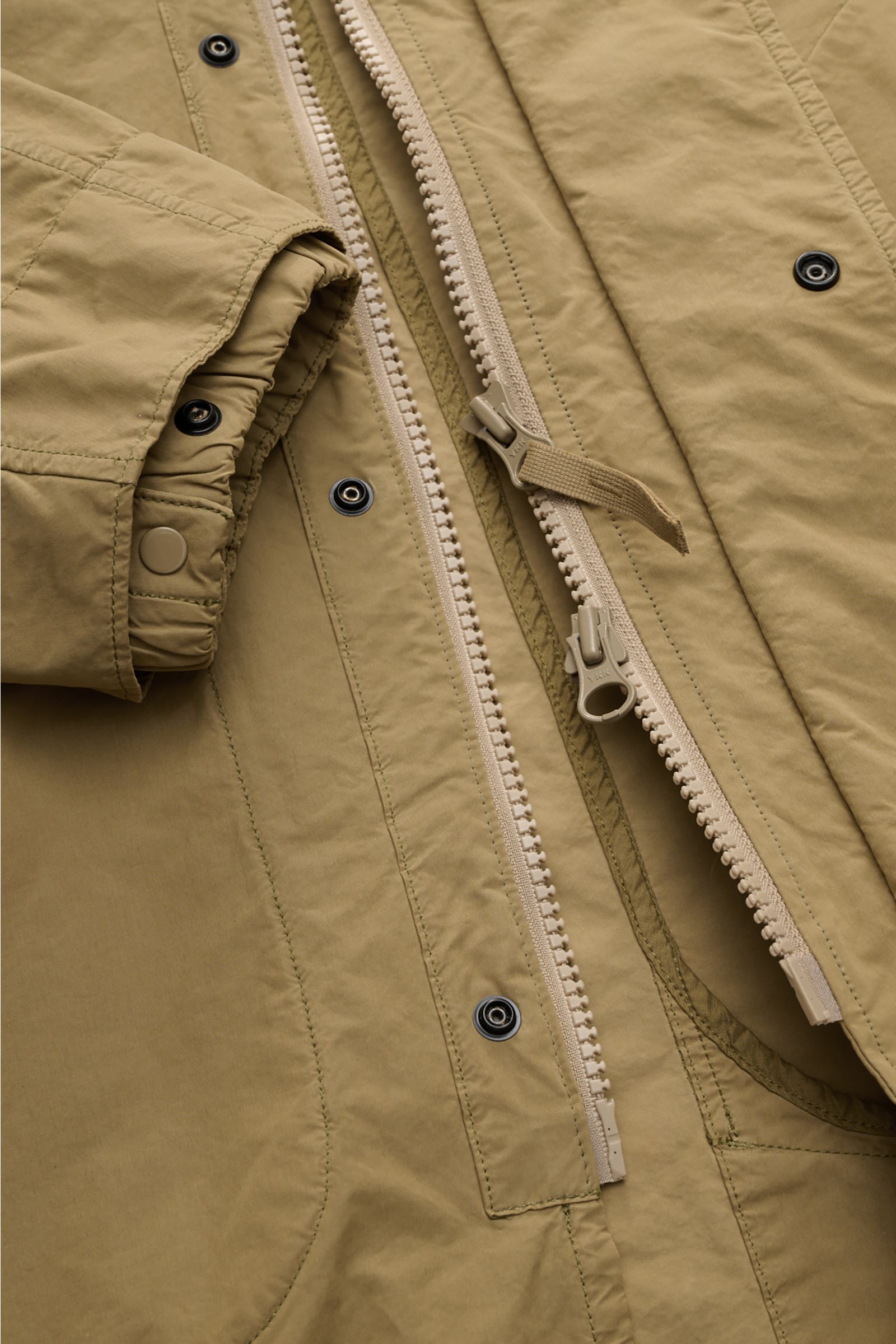 Close-up front view of the Stone Island Coat 'Ghost Piece' khaki showcasing the two-way zipper, snap buttons, and adjustable cuffs in lightweight, water-repellent microfibre fabric.