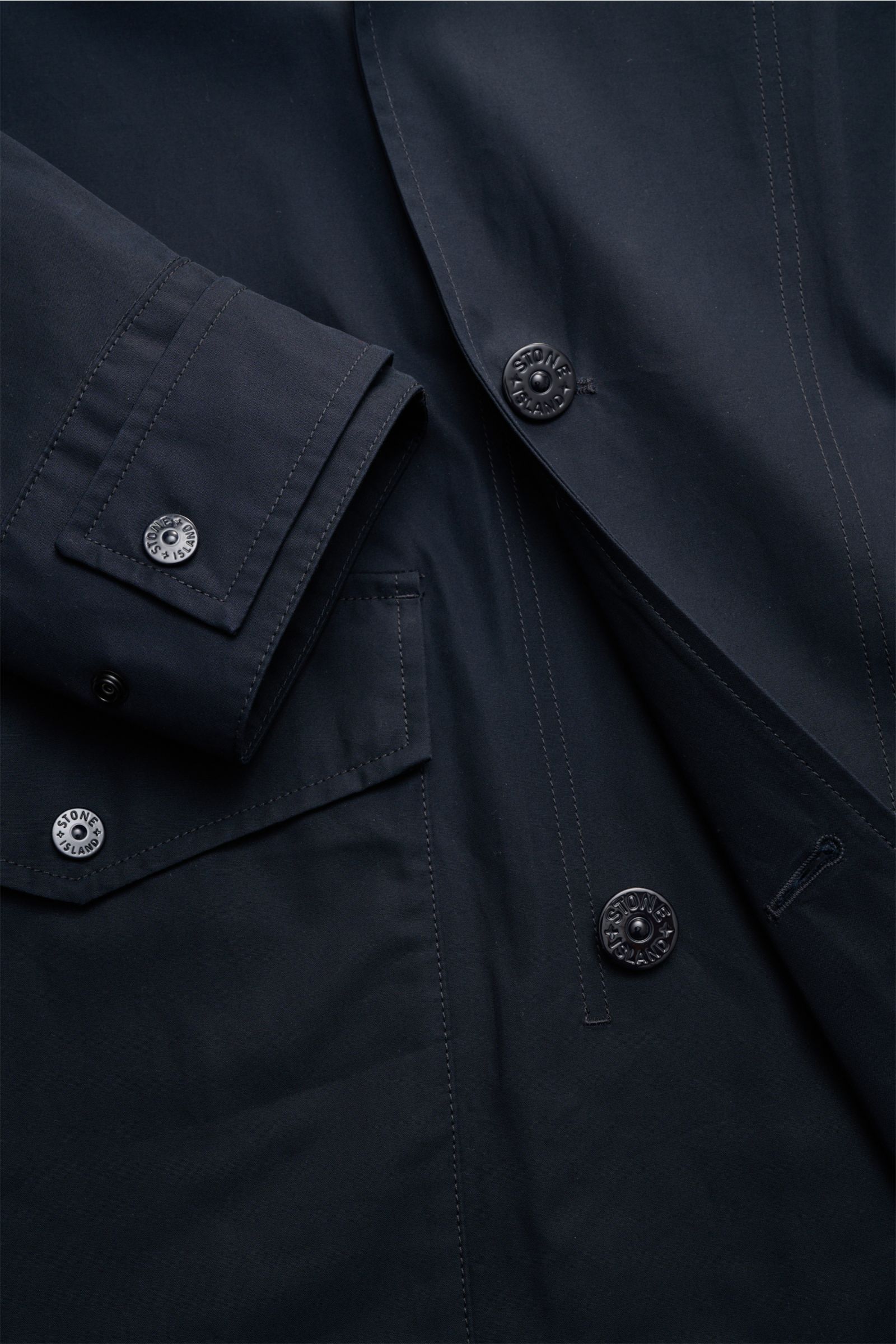 Close-up front view of Stone Island Kurzmantel 'Ghost Piece' navy showing water-repellent popeline, tonal buttons, and flap pocket details. Eleganz trifft Funktion: Der Kurzmantel von STONE ISLAND aus der 'Ghost-Collection' überzeugt mit wasserabweisendem