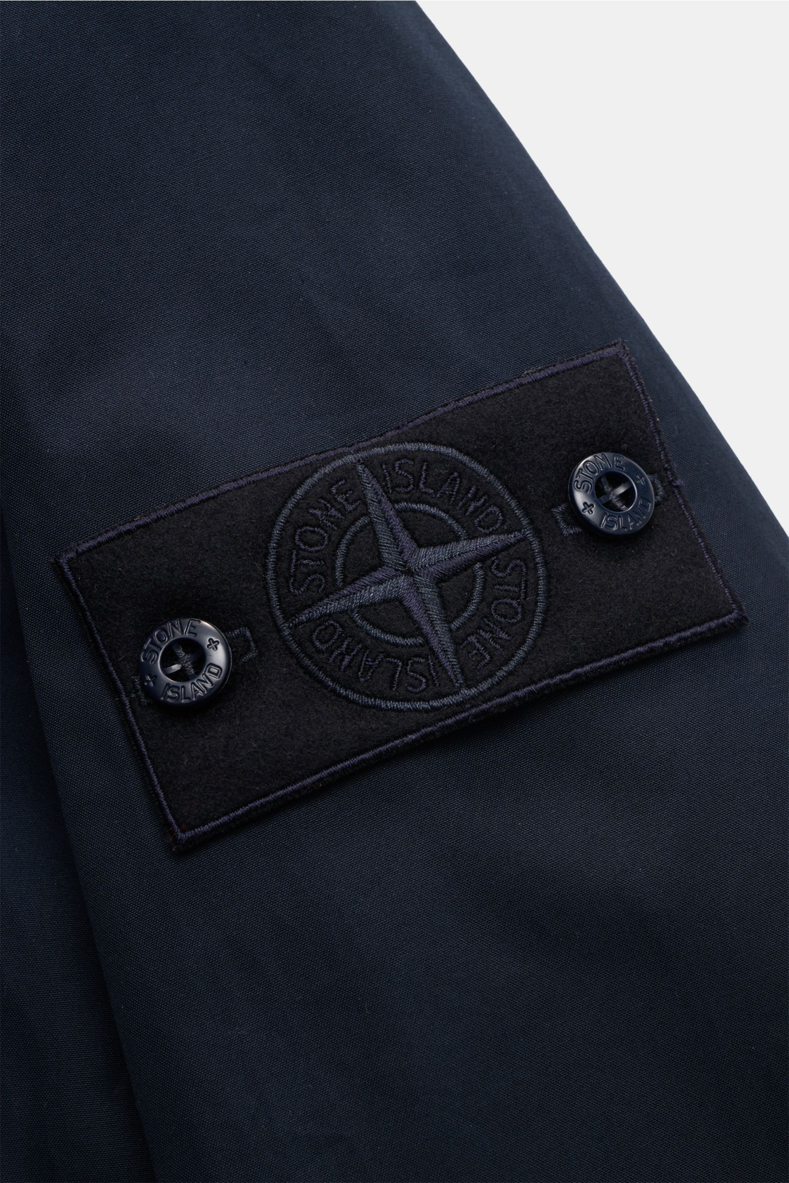 Close-up of the tonal compass badge on the sleeve of the Stone Island Kurzmantel 'Ghost Piece' navy, captured from a side angle.