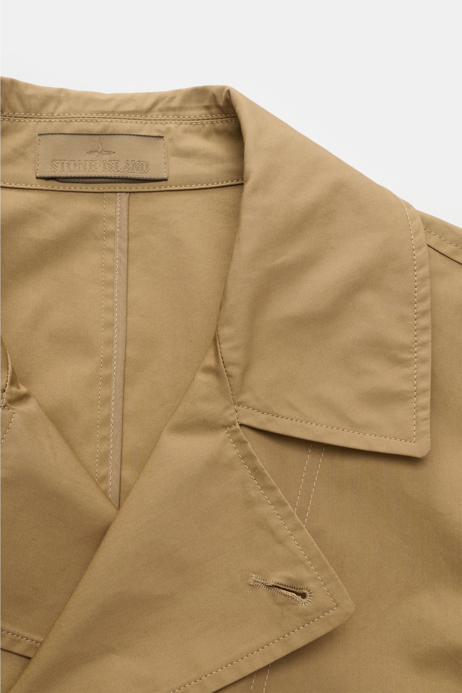 Close-up front top view of Stone Island Kurzmantel 'Ghost Piece' khaki, showing collar, lapel, and stitching details, highlighting elegant, water-repellent microfiber fabric and smooth texture. Elegance meets function with this slim fit coat featuring a t