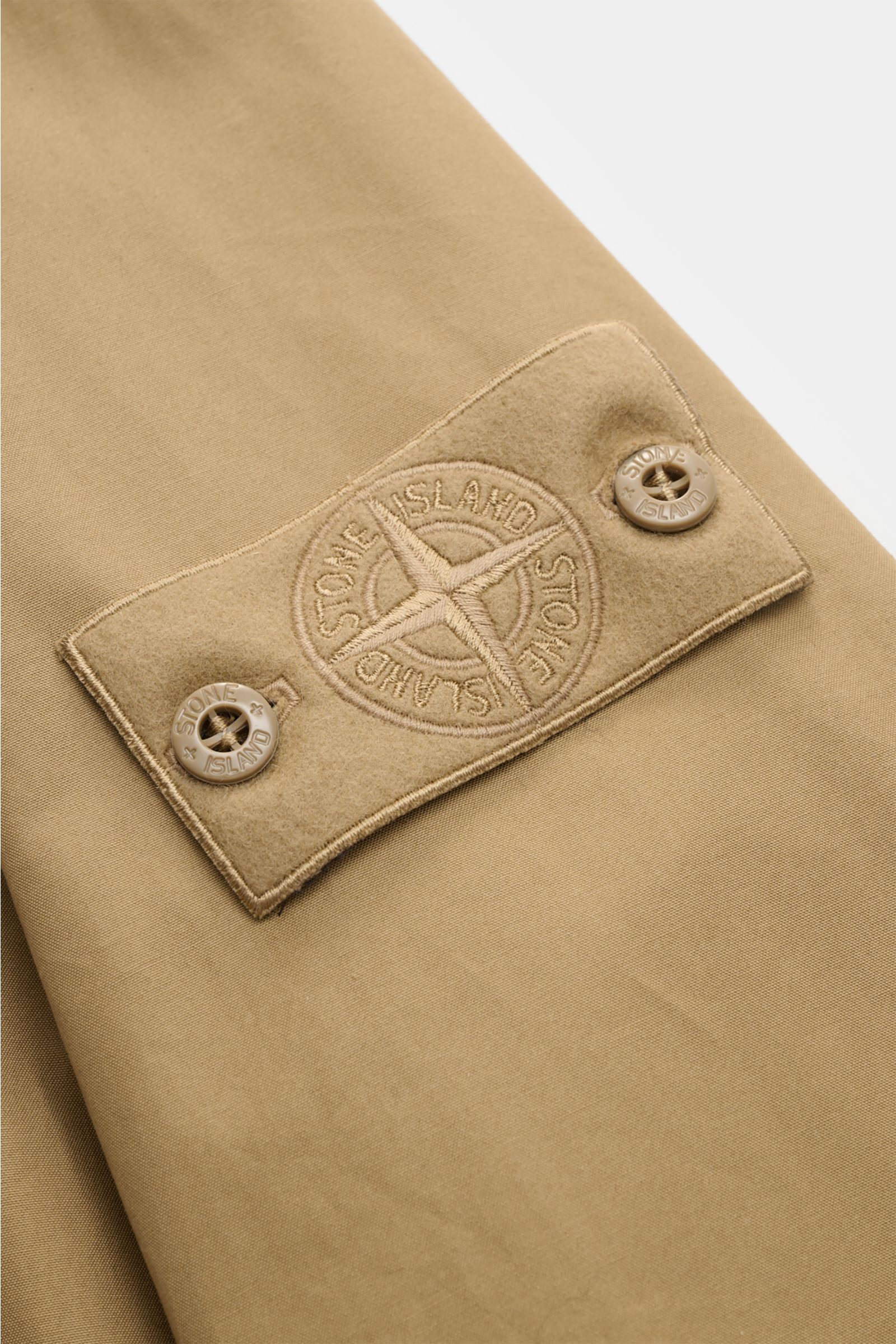 Close-up front view of Stone Island Kurzmantel 'Ghost Piece' khaki showing tonal compass badge on smooth, water-repellent microfiber fabric.

Eleganz trifft Funktion: Der Kurzmantel von STONE ISLAND aus der 'Ghost-Collection' überzeugt mit wasserabweis