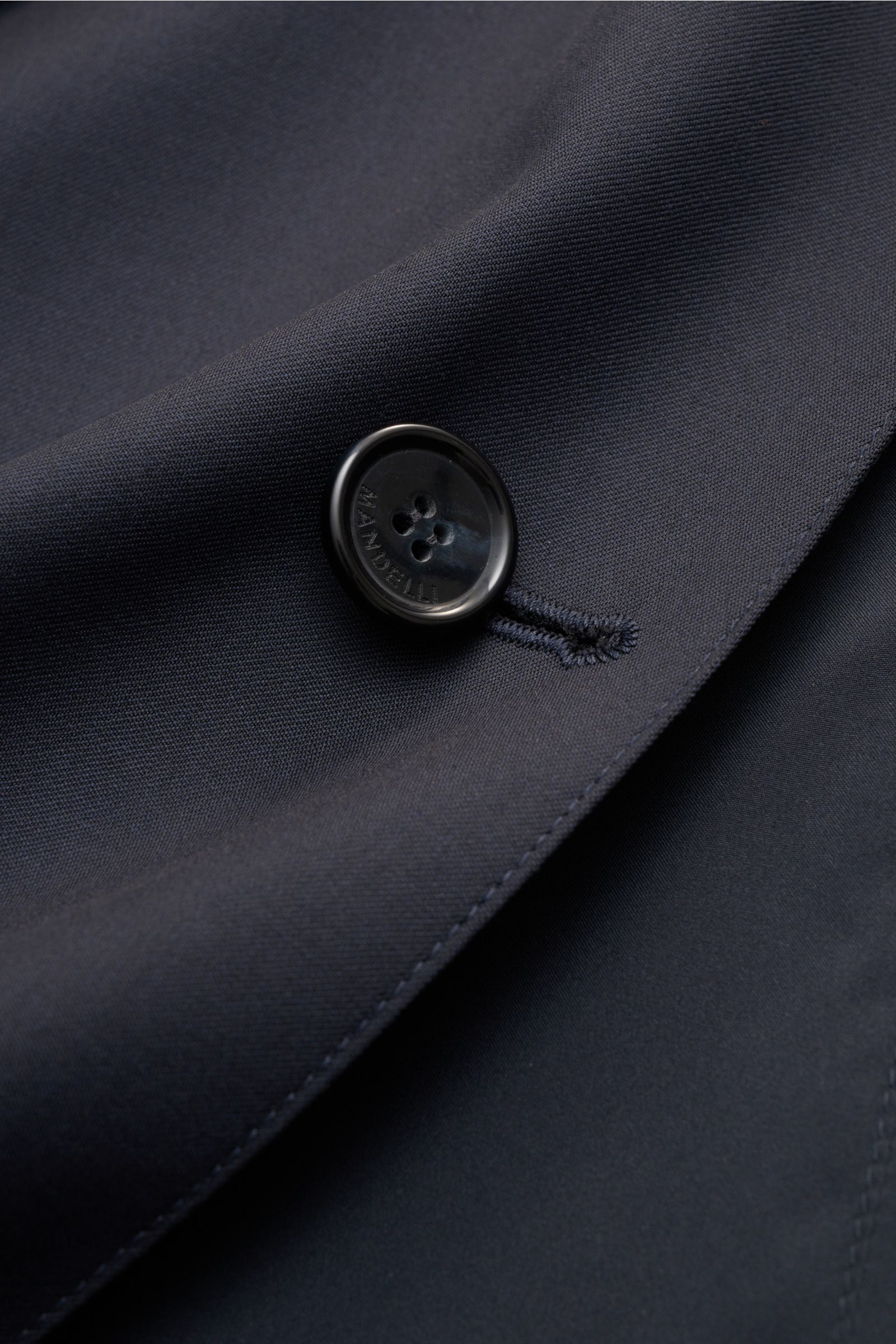 Nahaufnahme eines schwarzen Knopfes mit MANDELLI Prägung auf dem navy Stoff des Mandelli Wende-Kurzmantel navy aus reiner Wolle, weichem Griff, Slim Fit und Vier-Knopf-Leiste.