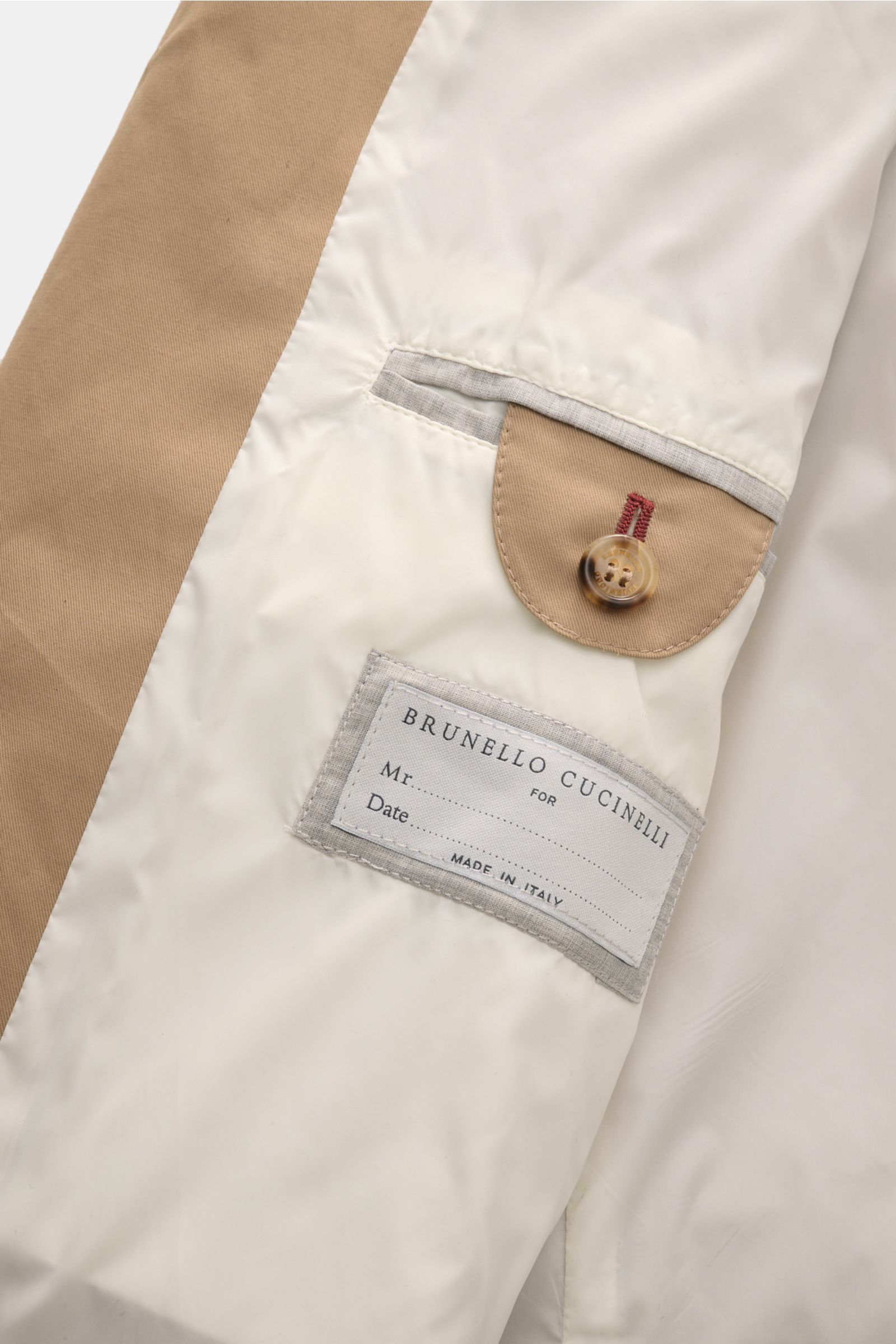 Close-up inner view of the beige Brunello Cucinelli Trenchcoat showing smooth lining, branded label, and buttoned pocket flap, photographed from above.

Wasserabweisend und atmungsaktiv: Ein innovativer Mix aus Baumwolle und Microfaser ist die Grundlag