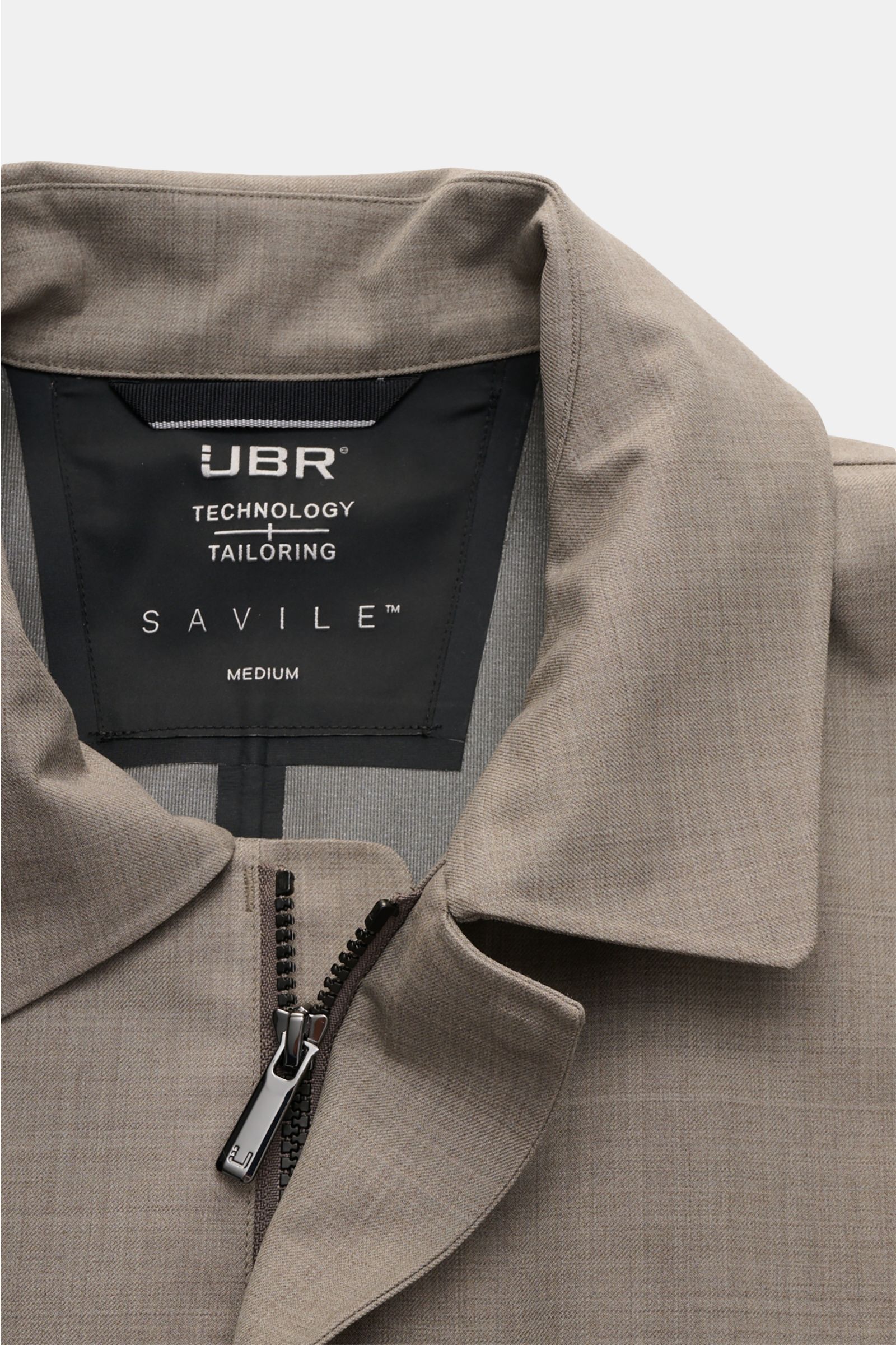 Close-up front view of UBR Rain coat 'Sky Fall Savile' taupe mottled, showing collar, zipper, and inner label with branding.

The incredibly lightweight rain coat 'Sky Fall Savile' by UBR is made of smart merino wool and microfibre for effortless prote