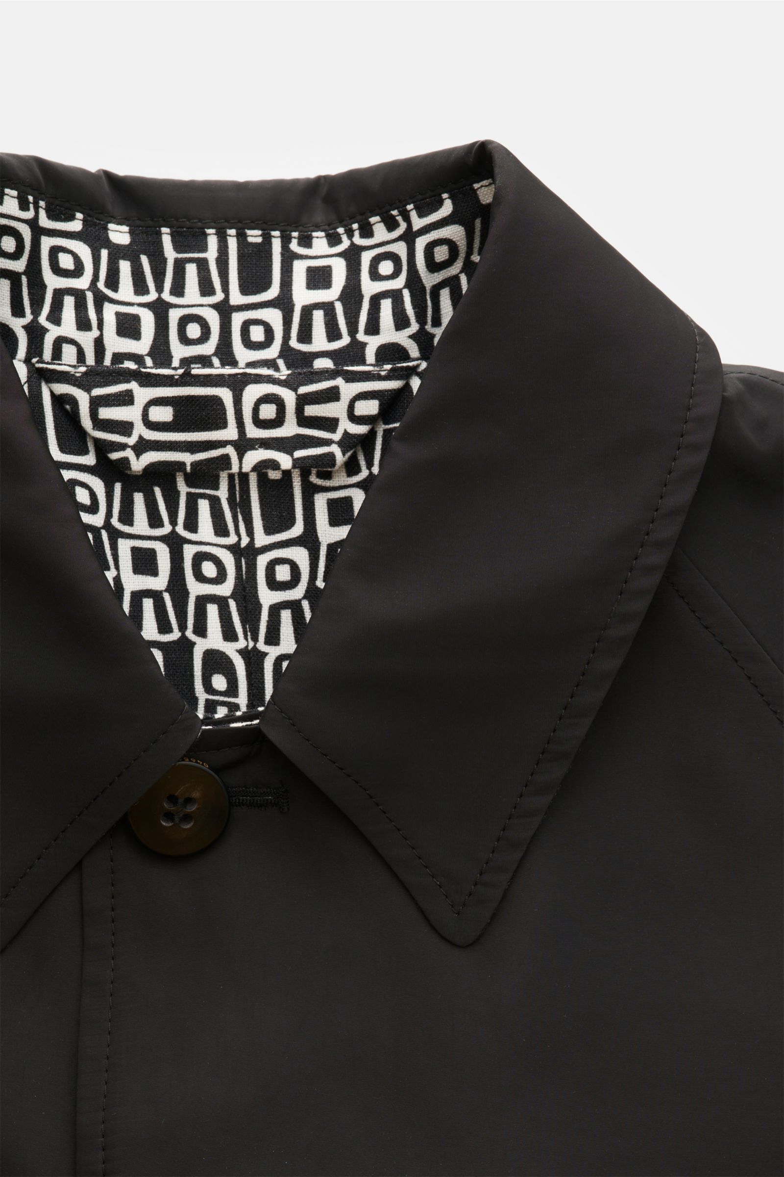 Nahaufnahme des 04651/ A trip in a bag Wende-Mantel 'Abstract' schwarz/offwhite mit Umlegekragen, Knopf und grafischem Innenfutter, Vorderansicht.