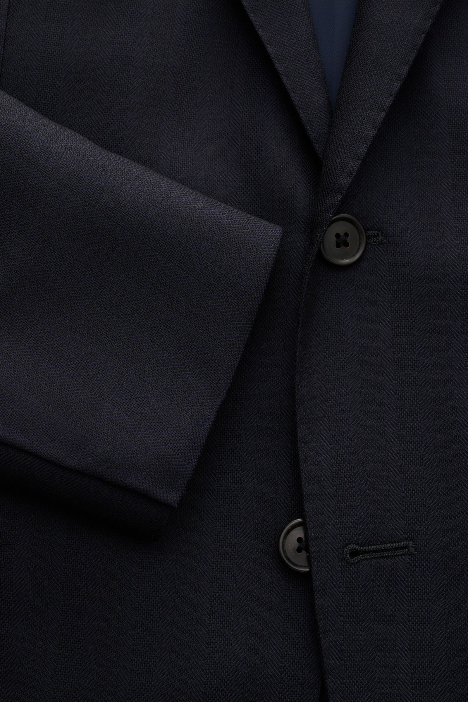 Corneliani Anzug dark navy aus reiner Schurwolle, Slim Fit, tonaler Fischgrat, frontale Nahaufnahme von Sakko mit Zwei-Knopf-Stil und fallendem Revers.