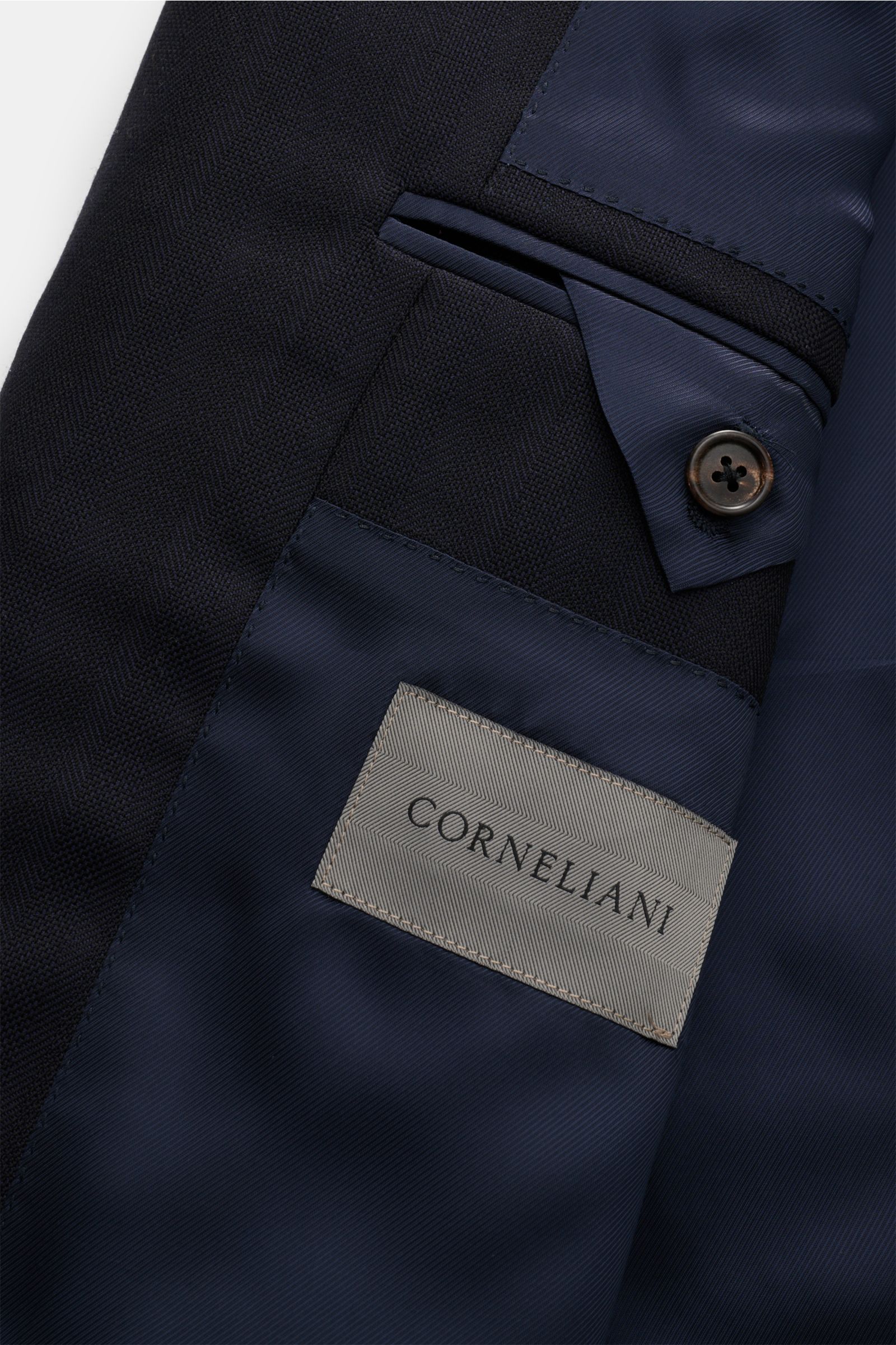 Corneliani Anzug dark navy, Detailaufnahme innen, reine Schurwolle, tonaler Fischgrat, weicher Griff, mit Label und Knopf, edle Verarbeitung.