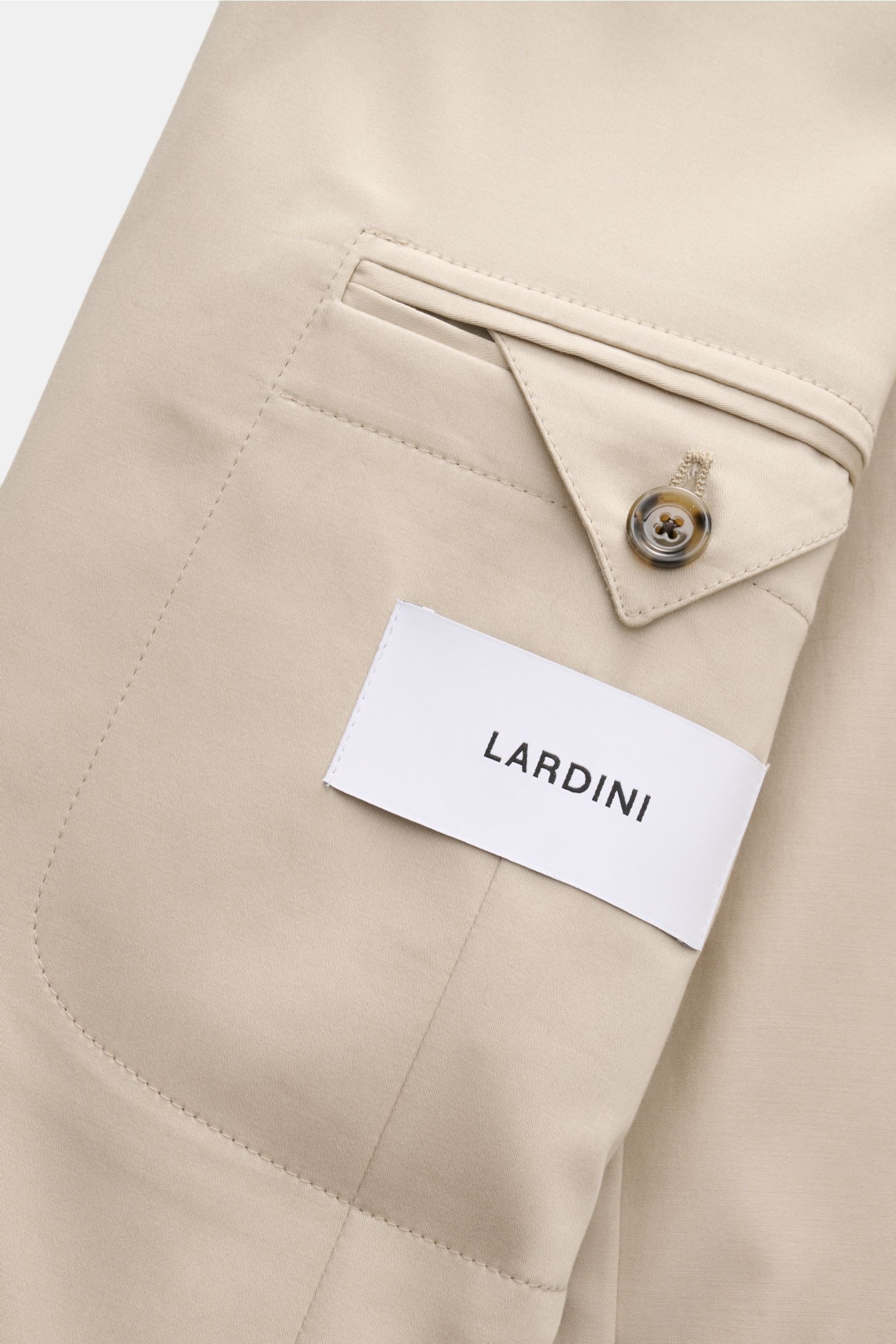 Nahaufnahme der Tasche eines Lardini Anzug beige aus elastischer Baumwolle mit weichem Griff, Detailansicht von Knopf und Label, seitliche Perspektive.