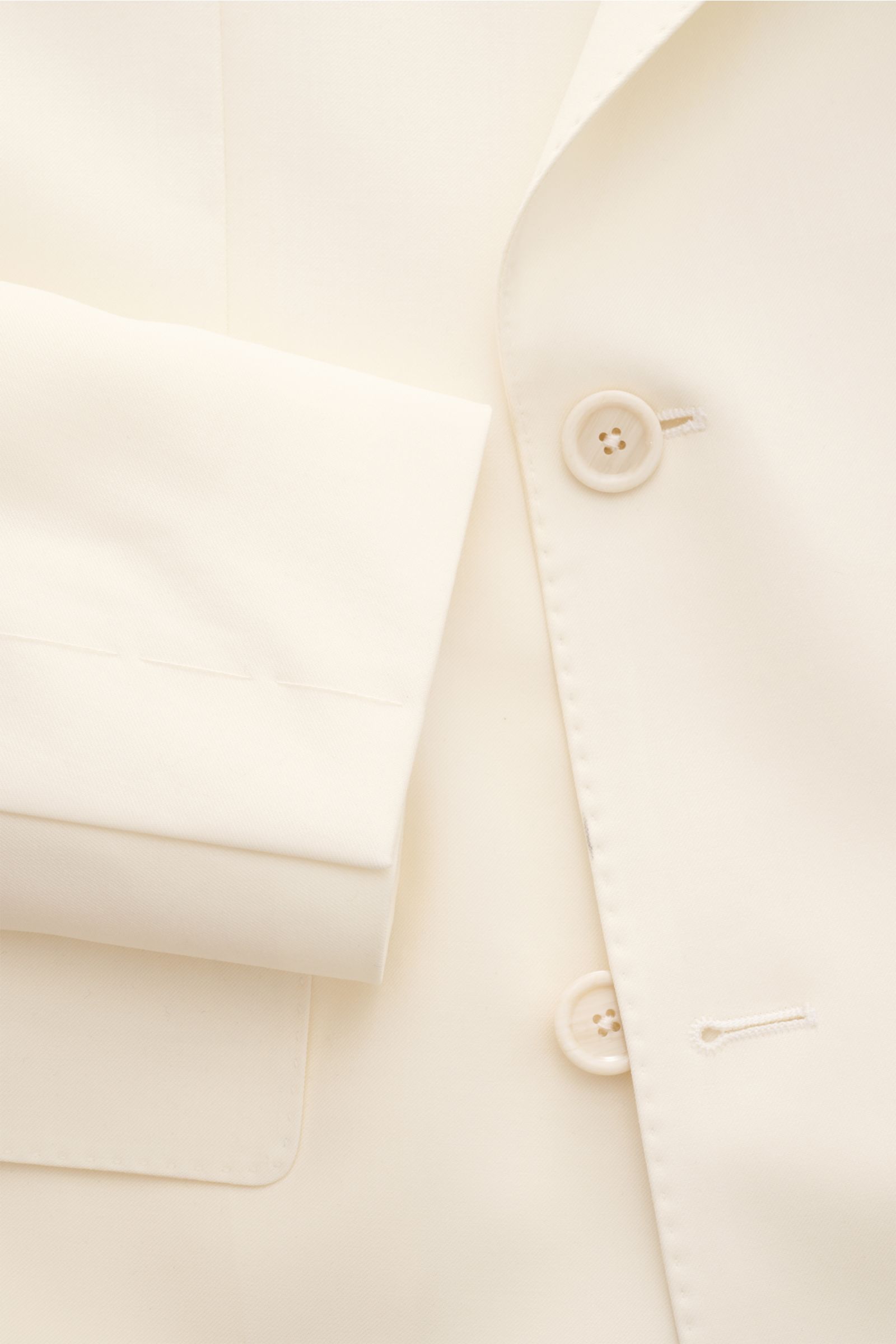 Close-up front view of the Lardini Anzug creme jacket sleeve and buttons, made of pure new wool with a soft touch, featuring slim fit, two-button style, and floral pin on the iconic lapel.
