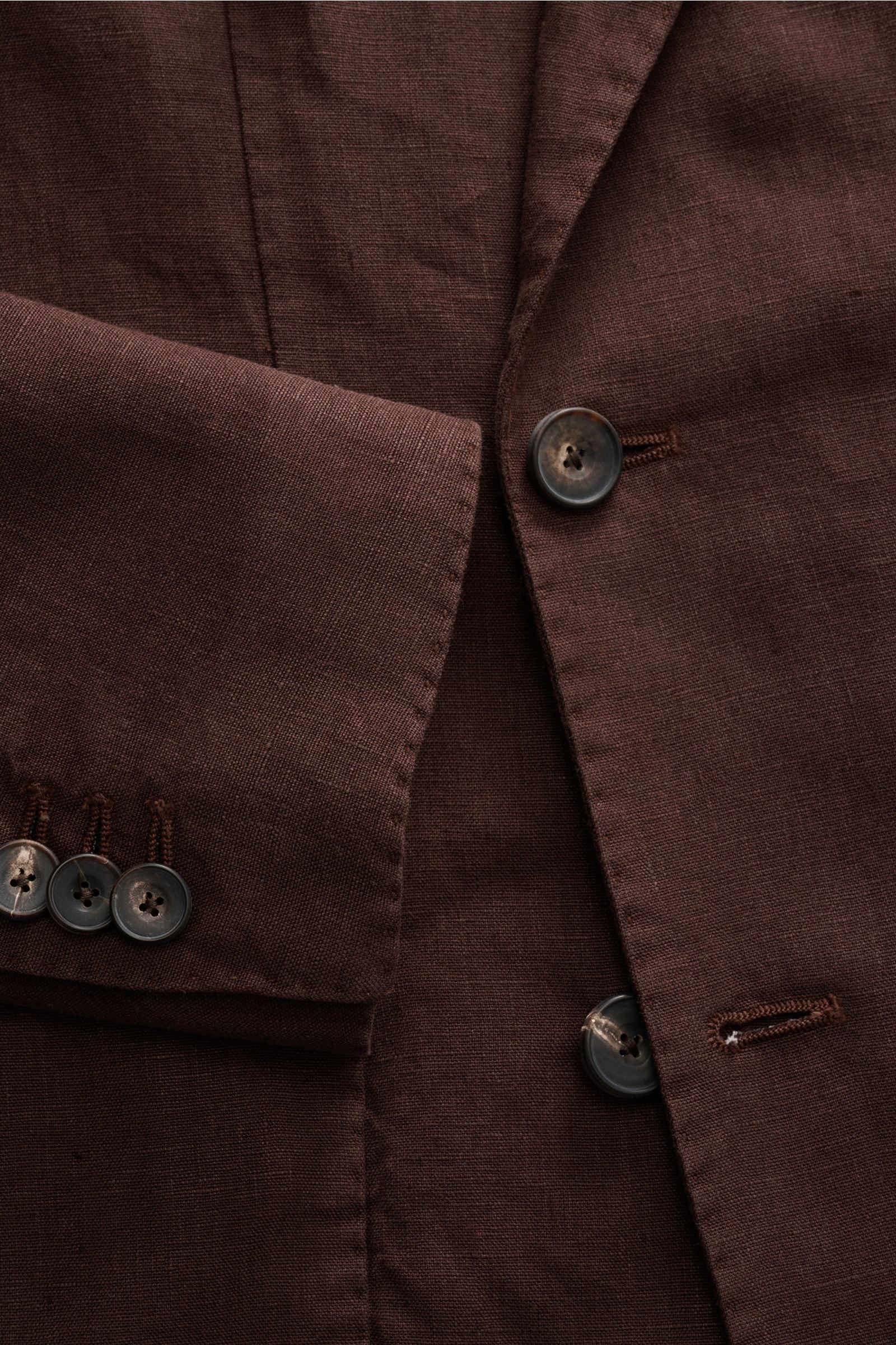 Nahaufnahme des braunen Santaniello Anzugs aus reinem Leinen, die taillierte Knopfleiste und Ärmel mit Kissing Buttons zeigt, vintage-inspirierter Slim Fit, fotografiert aus leicht seitlicher Frontperspektive.