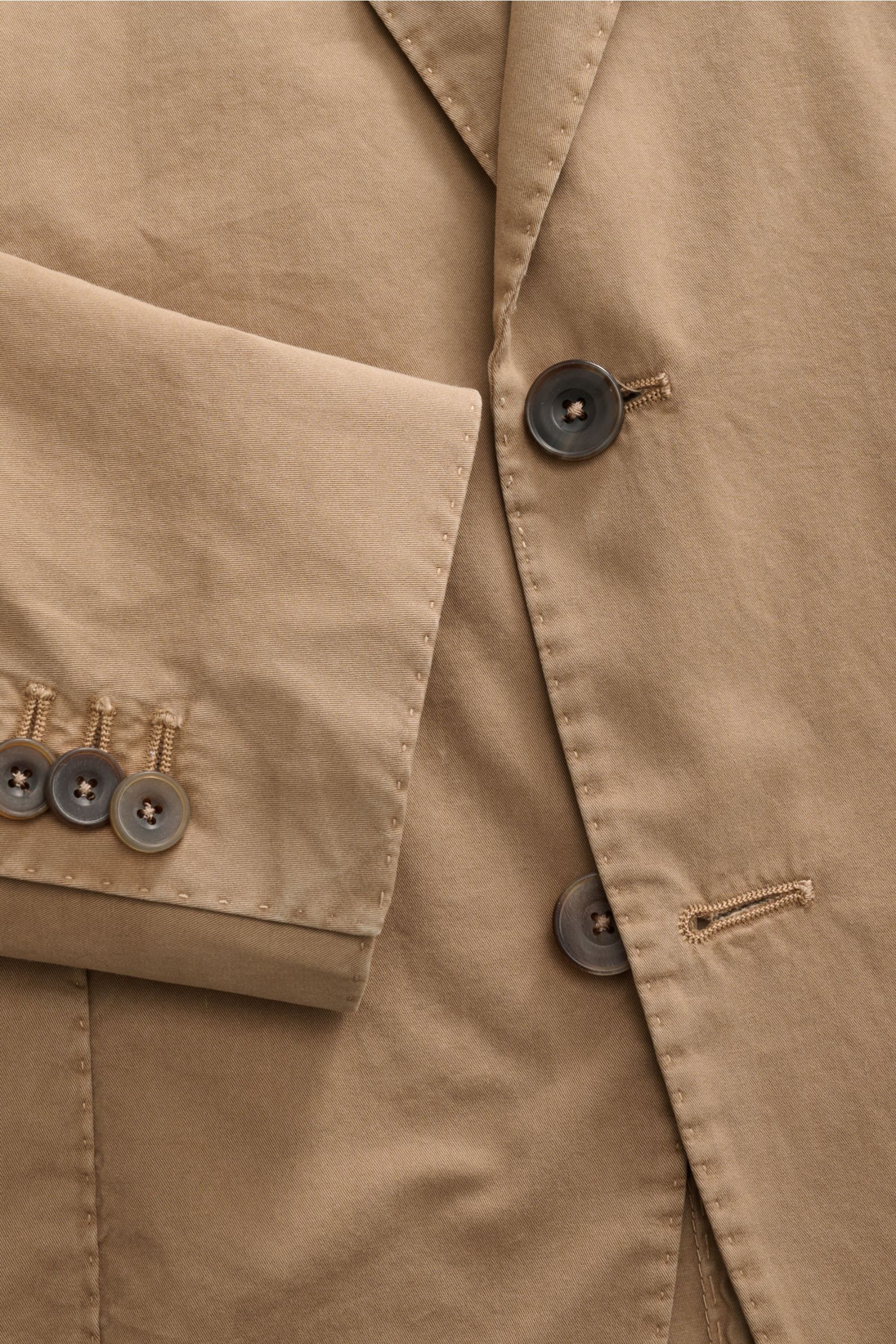Nahaufnahme des Santaniello Anzug taupe aus Baumwoll-Twill, Fokus auf tailliertes Sakko mit Knöpfen, fallendem Revers und Ärmel mit Kissing Buttons.