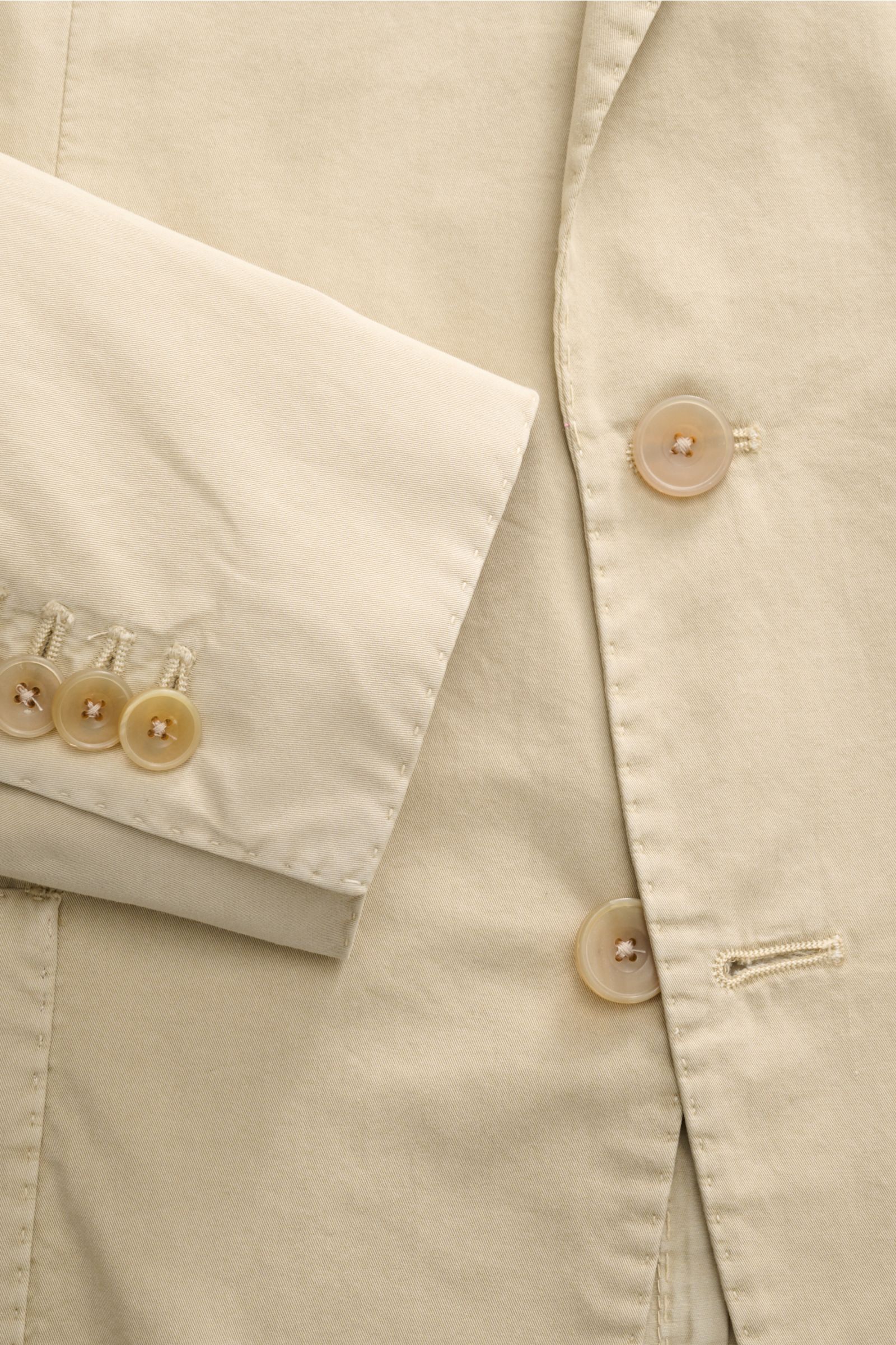 Close-up top-down view of the Santaniello Anzug sand jacket sleeve and front button area, showcasing fine cotton twill fabric and buttons. Lässige Eleganz mit Stil: Dieser Anzug von SANTANIELLO überzeugt mit feinstem Baumwoll-Twill und modernem Design - i