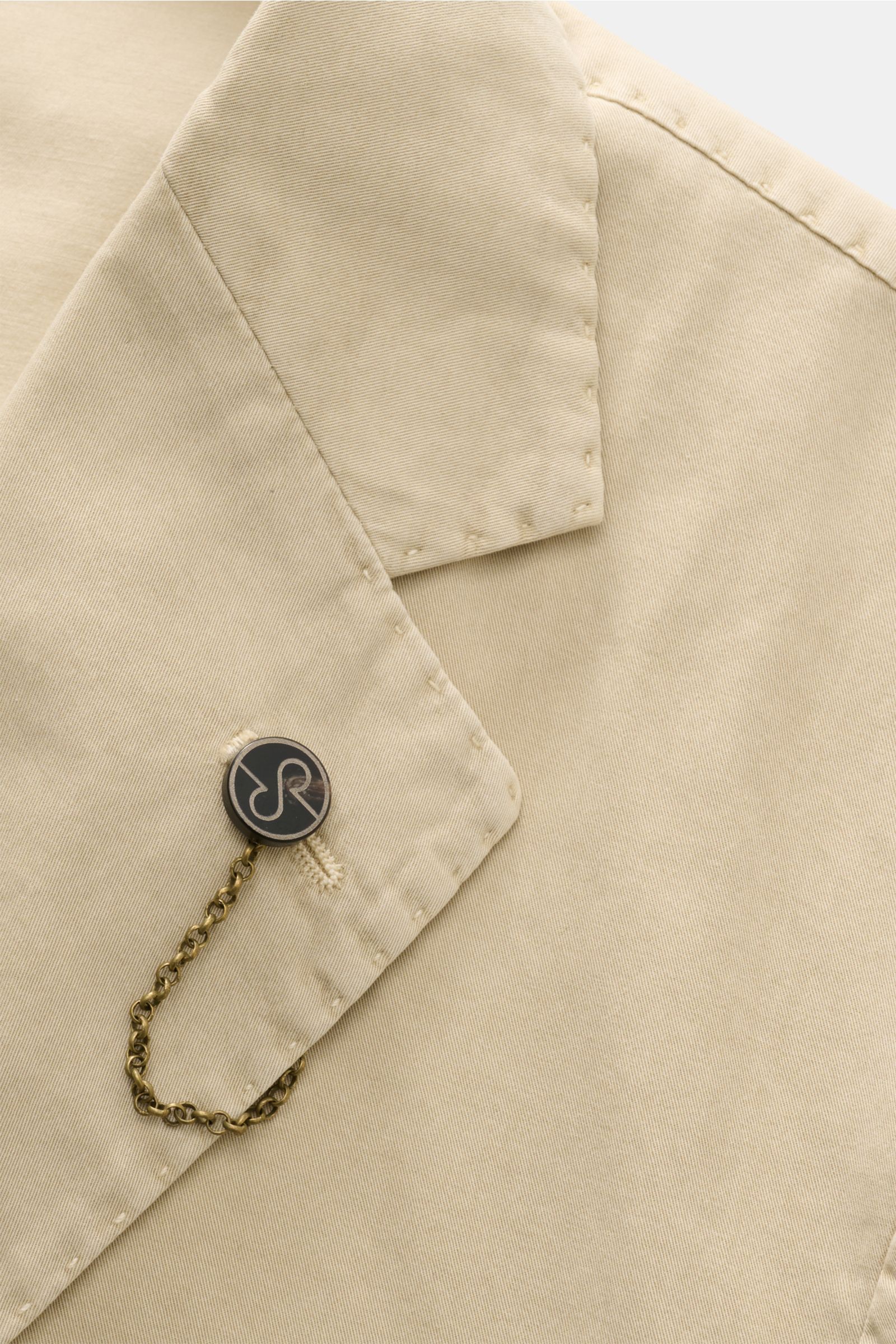 Close-up, top-down view of the Santaniello Anzug sand, showing the fine cotton twill fabric, soft texture, tailored two-button lapel, with a decorative chain and button detail. Lässige Eleganz mit Stil: Dieser Anzug von SANTANIELLO überzeugt mit feinstem 