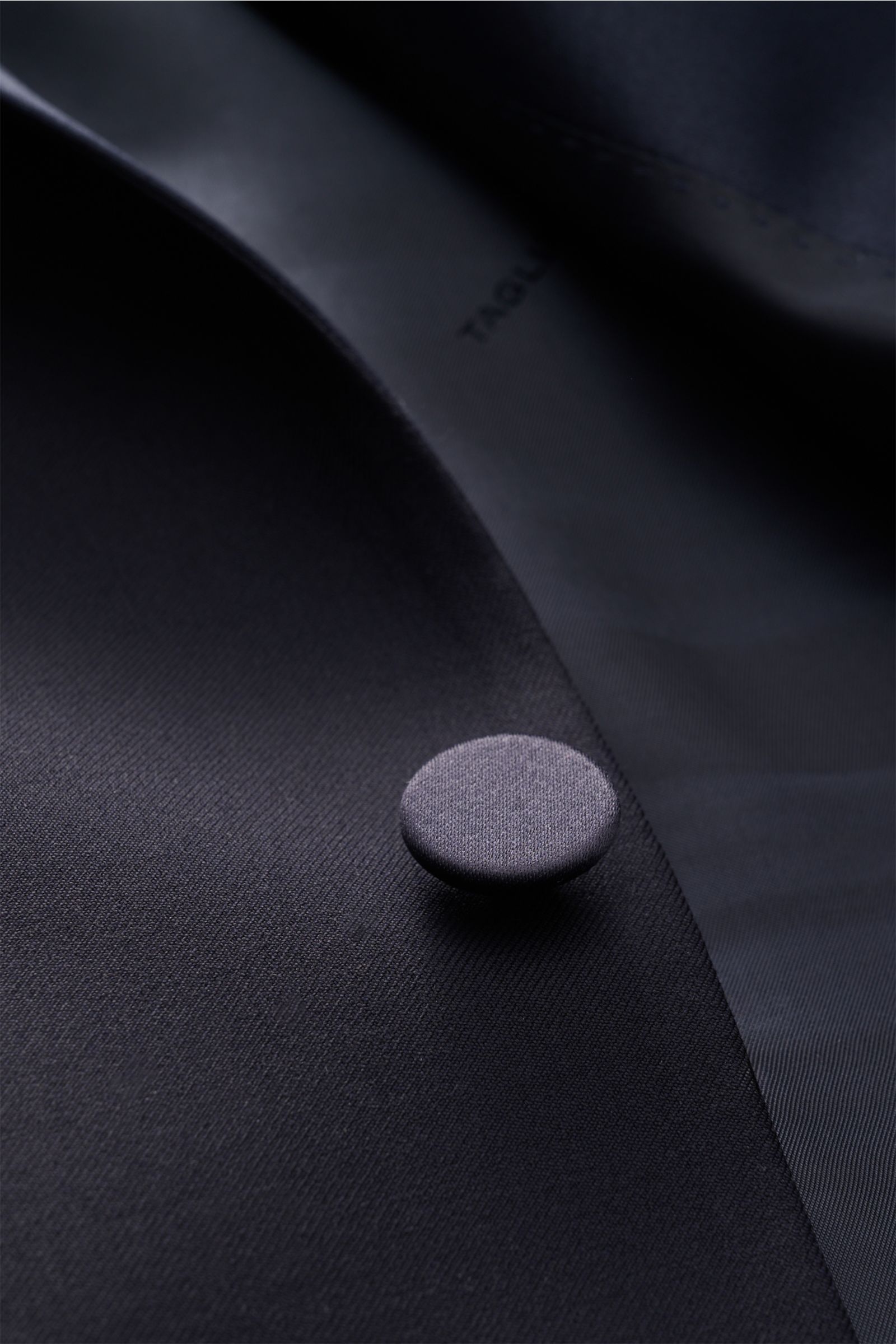 Close-up front angle of navy fabric and button detail on the Tagliatore Tuxedo navy, Italian evening wear in pure Super 110'S virgin wool. Italian evening wear for elegant occasions: Draw attention to yourself in style with this classy tuxedo in pure Supe