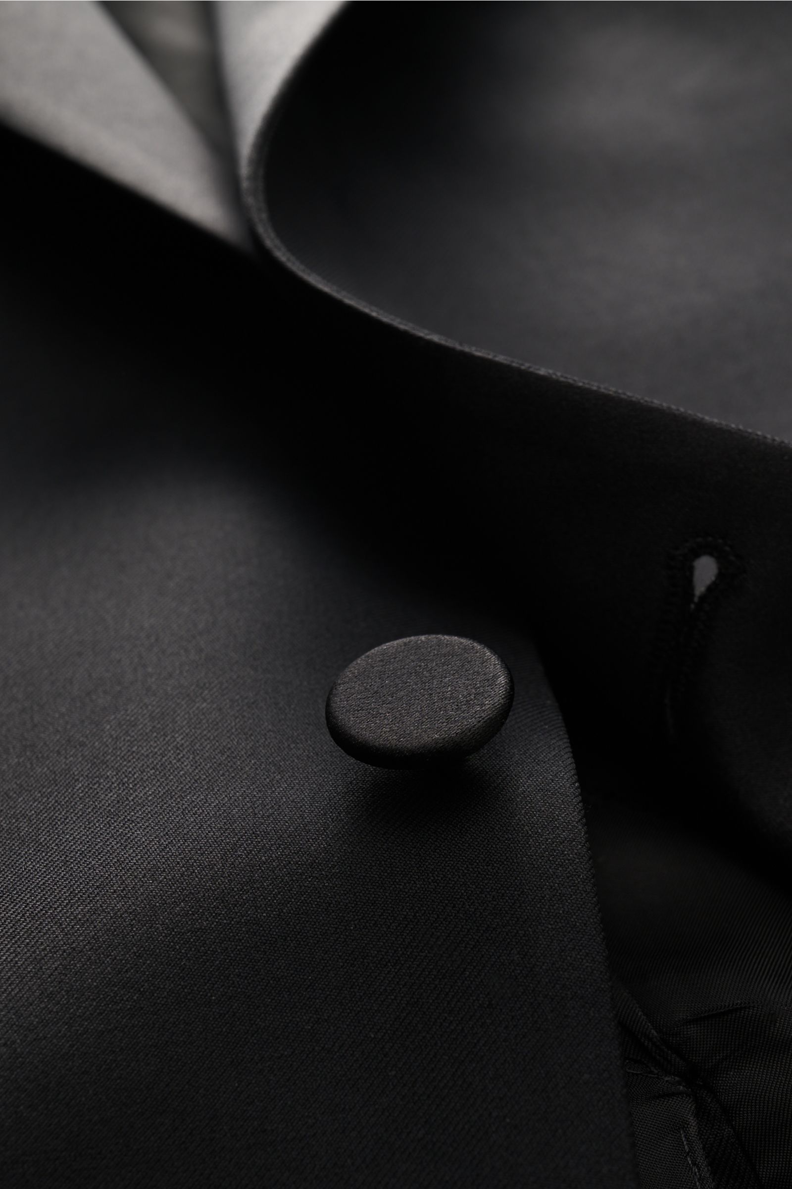 Close-up front detail of the Tagliatore Tuxedo black button and lapel, photographed from a slightly angled top view, showcasing the pure Super 110'S virgin wool fabric with a smooth feel and slim fit.