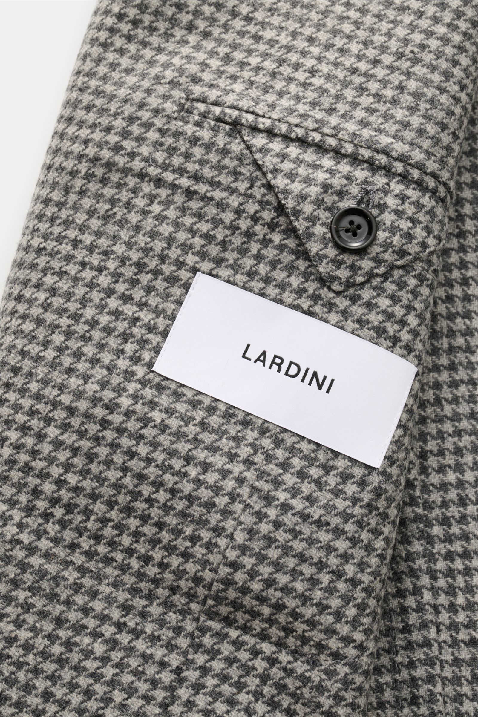 Close-up image of the sleeve and pocket of the Lardini Sakko hellgrau/dunkelgrau kariert, showing the grey Glencheck pattern and button, photographed from a top angle. Ob im Office oder unterwegs – das Unconstructed-Sakko von LARDINI aus einer edlen Wo
