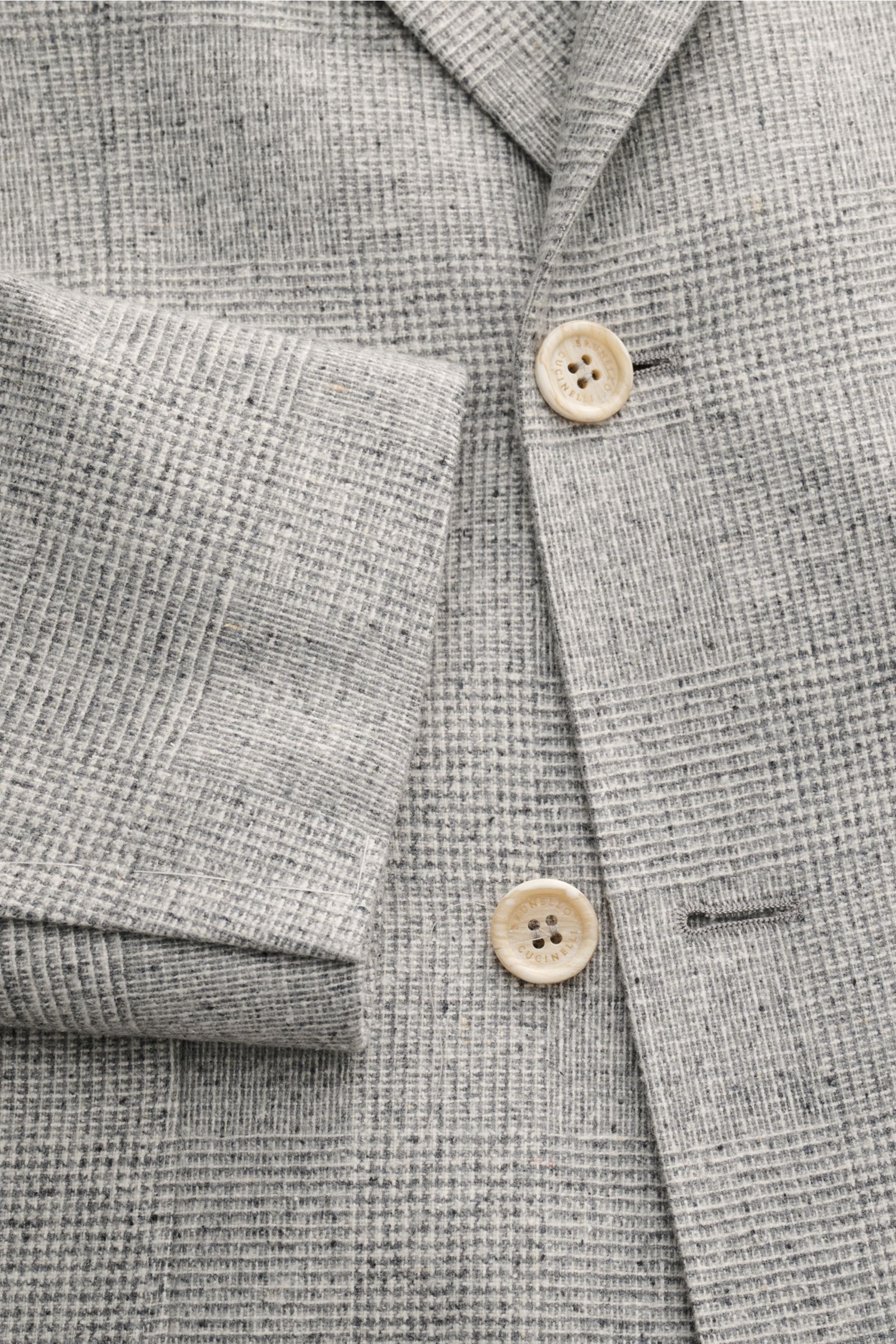 Close-up front view of the Brunello Cucinelli Sakko creme/grau kariert, showing its classic Glencheck pattern, soft silk, wool, and cashmere fabric, horn buttons, and slim fit details. Ganz klassisch, aber dennoch saisonal, kleiden Sie sich mit diesem 