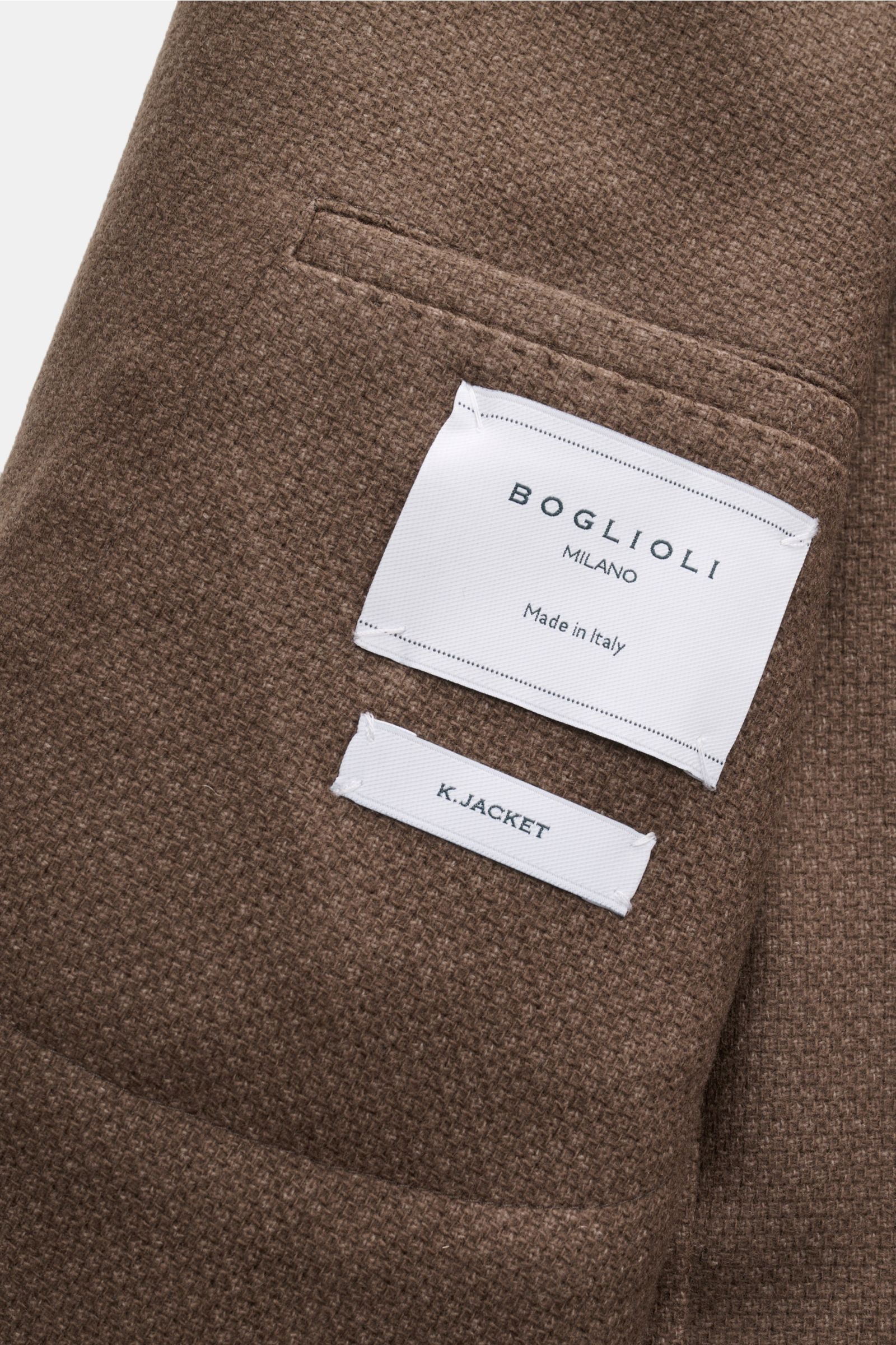Close-up image of the inside pocket with white labels on the graubraun meliert textured fabric of the Boglioli Sakko 'K. Jacket' photographed from above. Ideal für Business und Freizeit: Mit dem schlichten Unconstructed-Sakko 'K. Jacket' von BOGLIOLI a