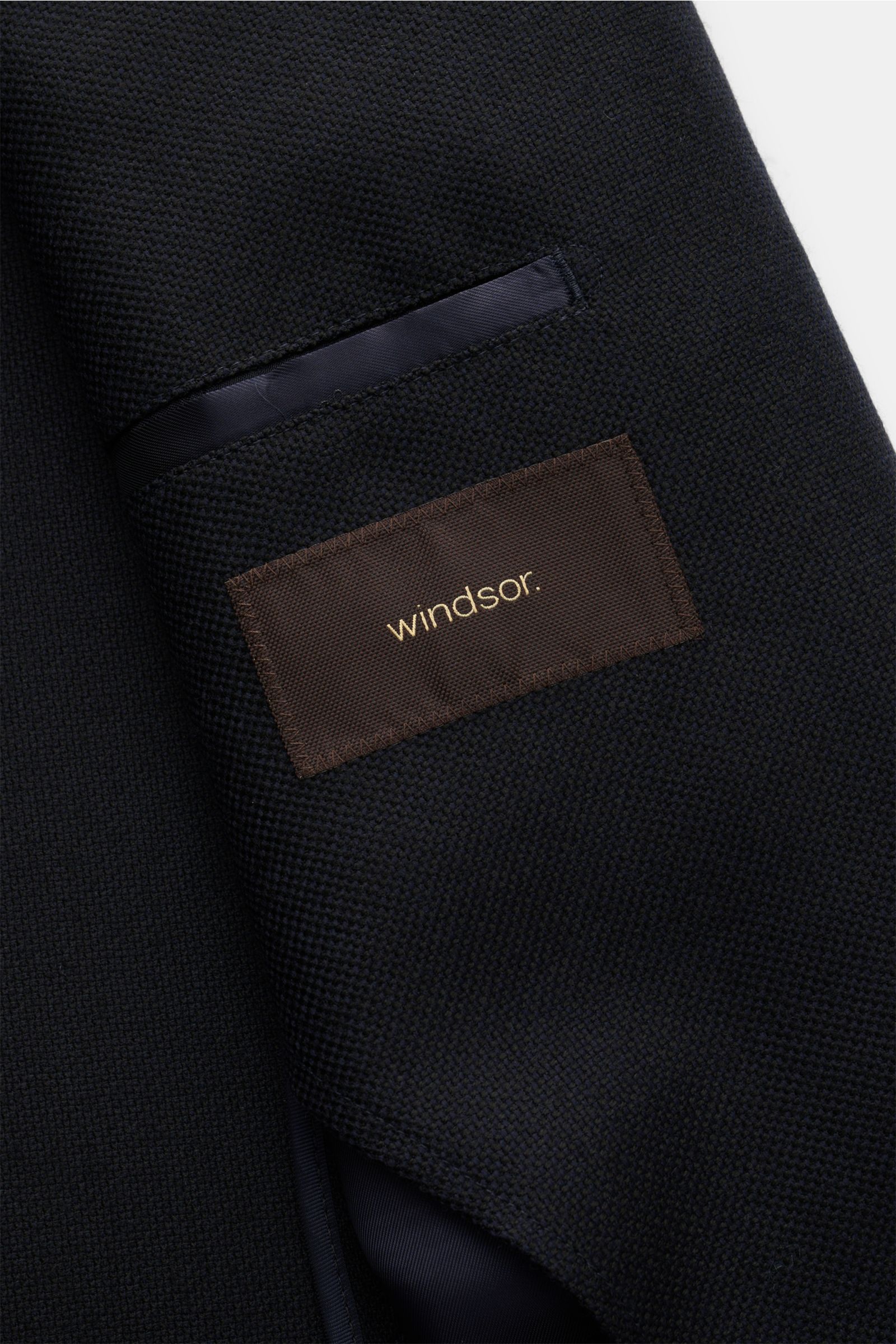 Close-up front view of Windsor Sakko 'Sora' dark navy jacket showing texture and interior pocket with brown label. Features: Panama aus reiner Wolle, weicher Griff, Slim Fit, fallendes Revers, Zwei-Knopf-Stil, klassische Brusttasche, aufgesetzte Hüfttasch