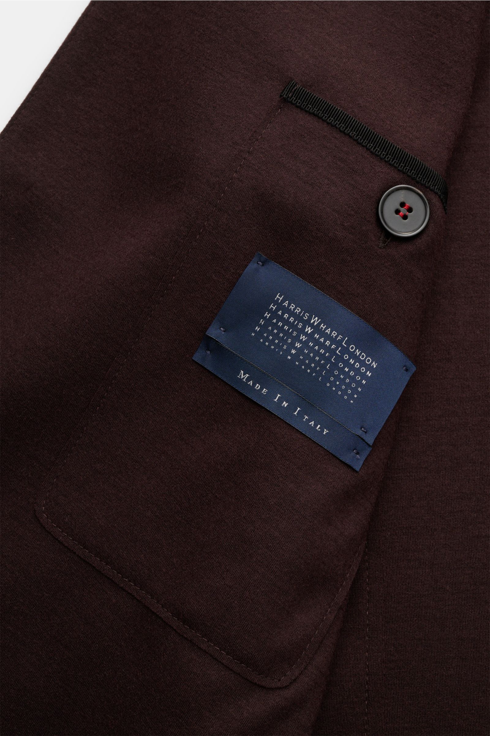 Close-up of the inside pocket and label of Harris Wharf London Jersey-Sakko dunkelbraun, showing dark brown wool jersey fabric, button, and stitching from a top-down perspective.

Description: Die elegante Optik eines Sakkos trift auf den Komfort einer