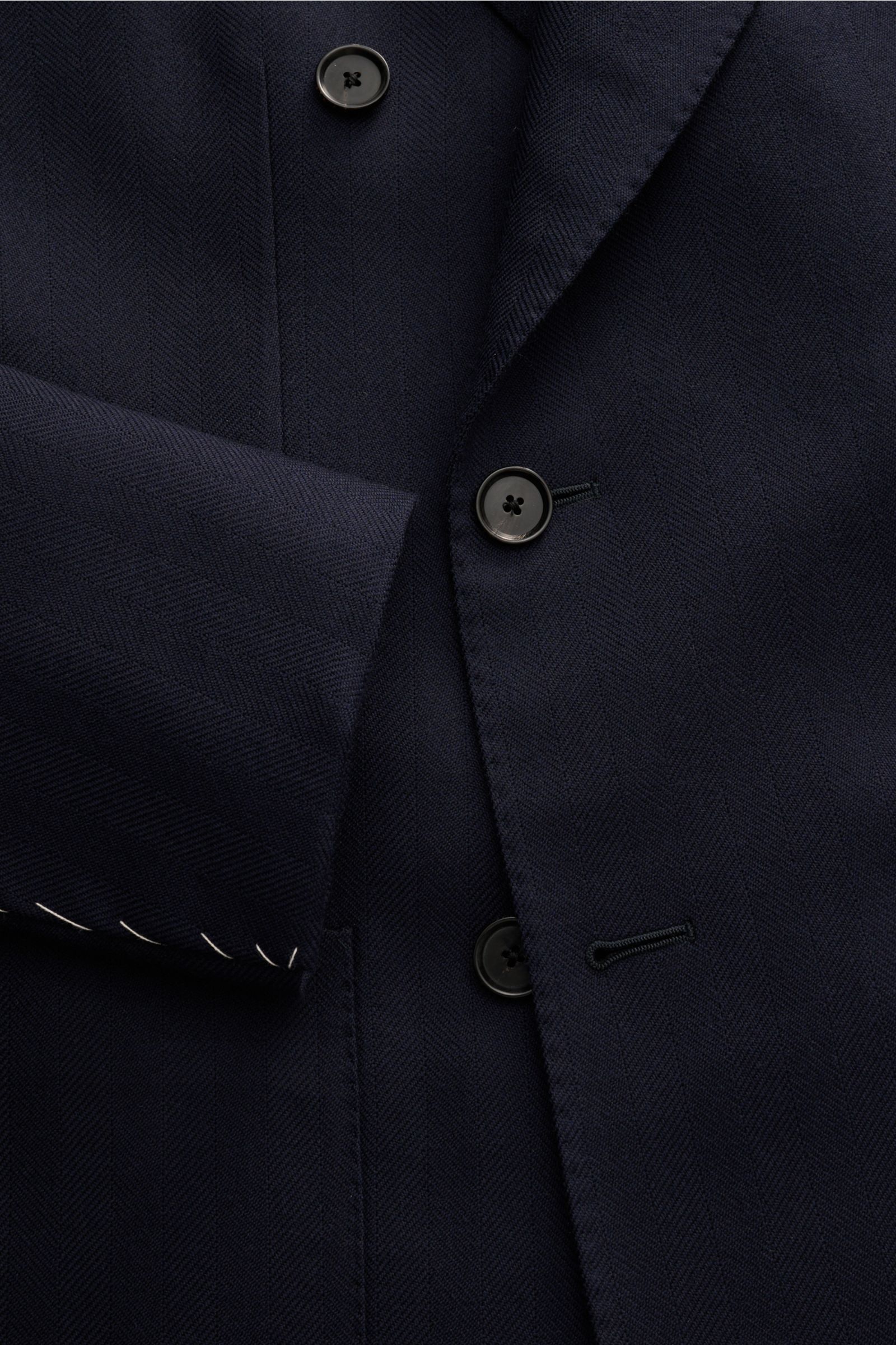 Close-up front view of the Caruso Sakko 'Aida' navy, showcasing fine wool fabric with tonal herringbone texture, slim fit, two-row three-button style, notch lapel, and unfinished sleeve cuffs. 

Feine Webstruktur, italienische Eleganz – das Sakko 'Aida