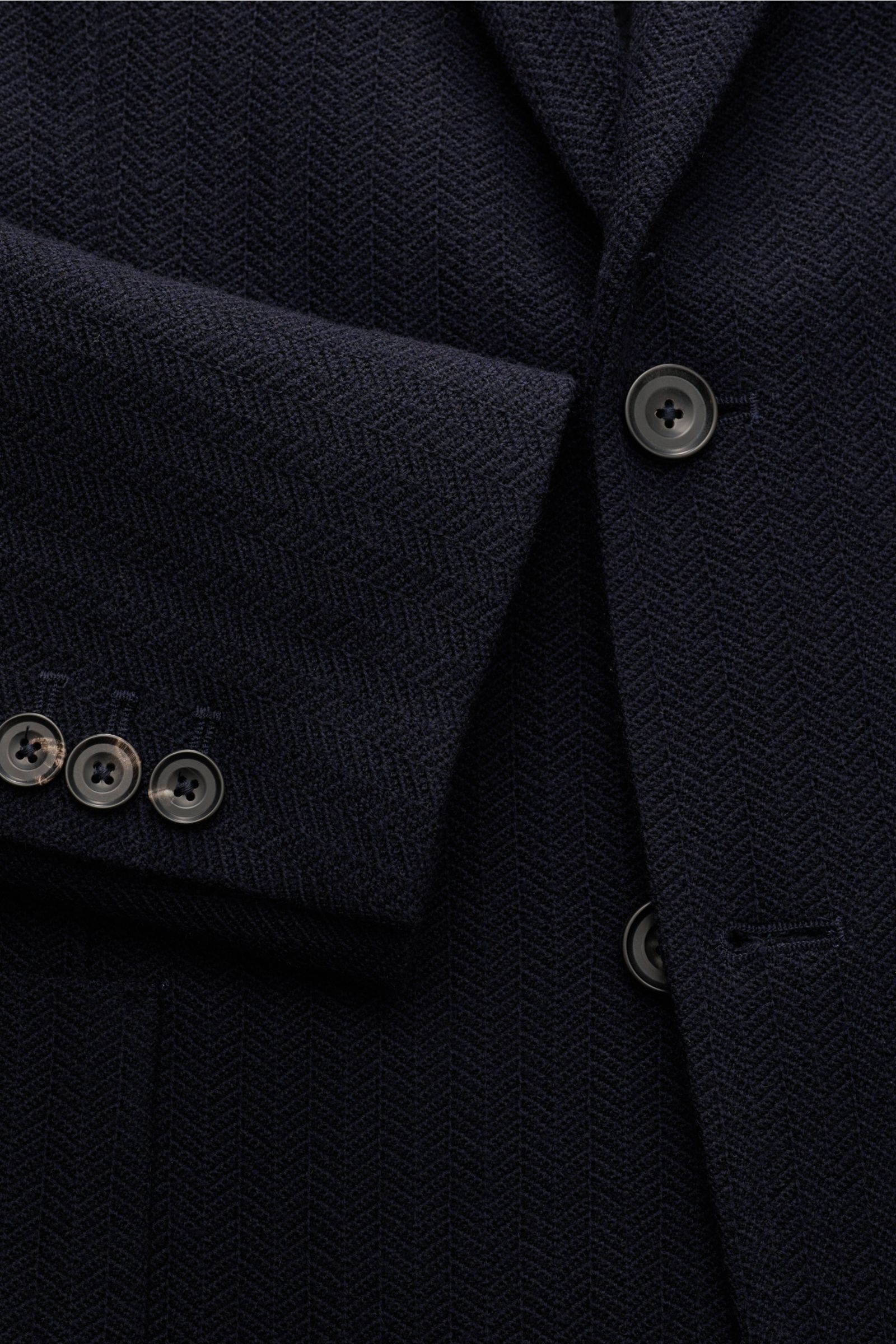 Nahaufnahme des Circolo 1901 Strickblazer navy aus reiner Wolle mit tonalem Fischgrat, zwei Knöpfen, fallendem Revers, Slim Fit, Brust- und Hüfttaschen, Knopfärmel, Seitenschlitzen und Unconstructed-Design, fotografiert aus seitlicher Perspektive.