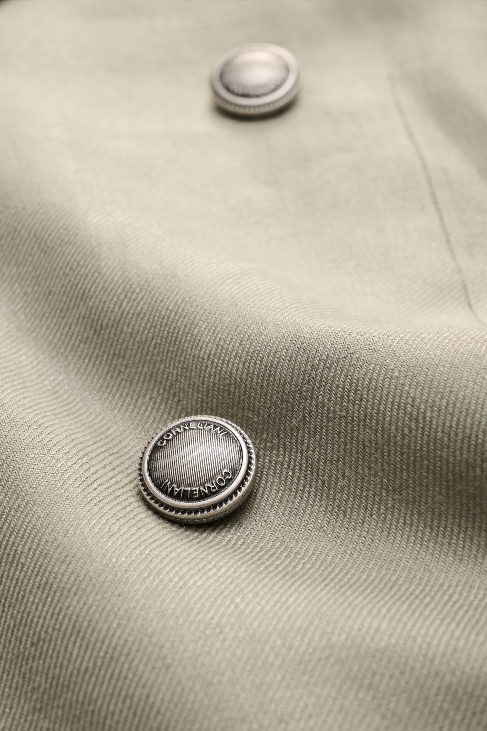 Nahaufnahme des Corneliani Leinensakko salbei mit Fokus auf Metallknöpfe und feine Leinenstruktur in weichem Griff.
